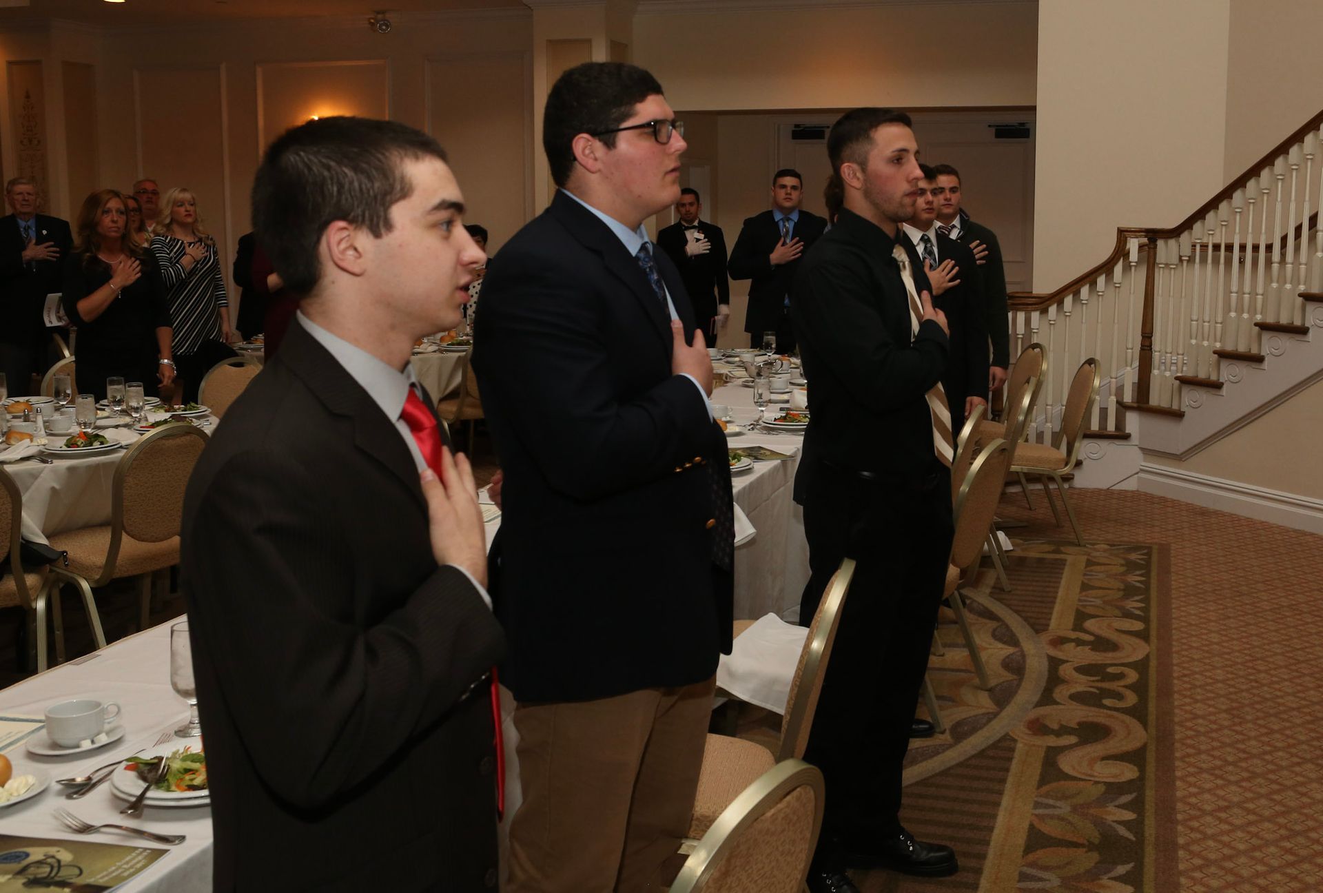 a group of men stand in a room with their hands on their hearts