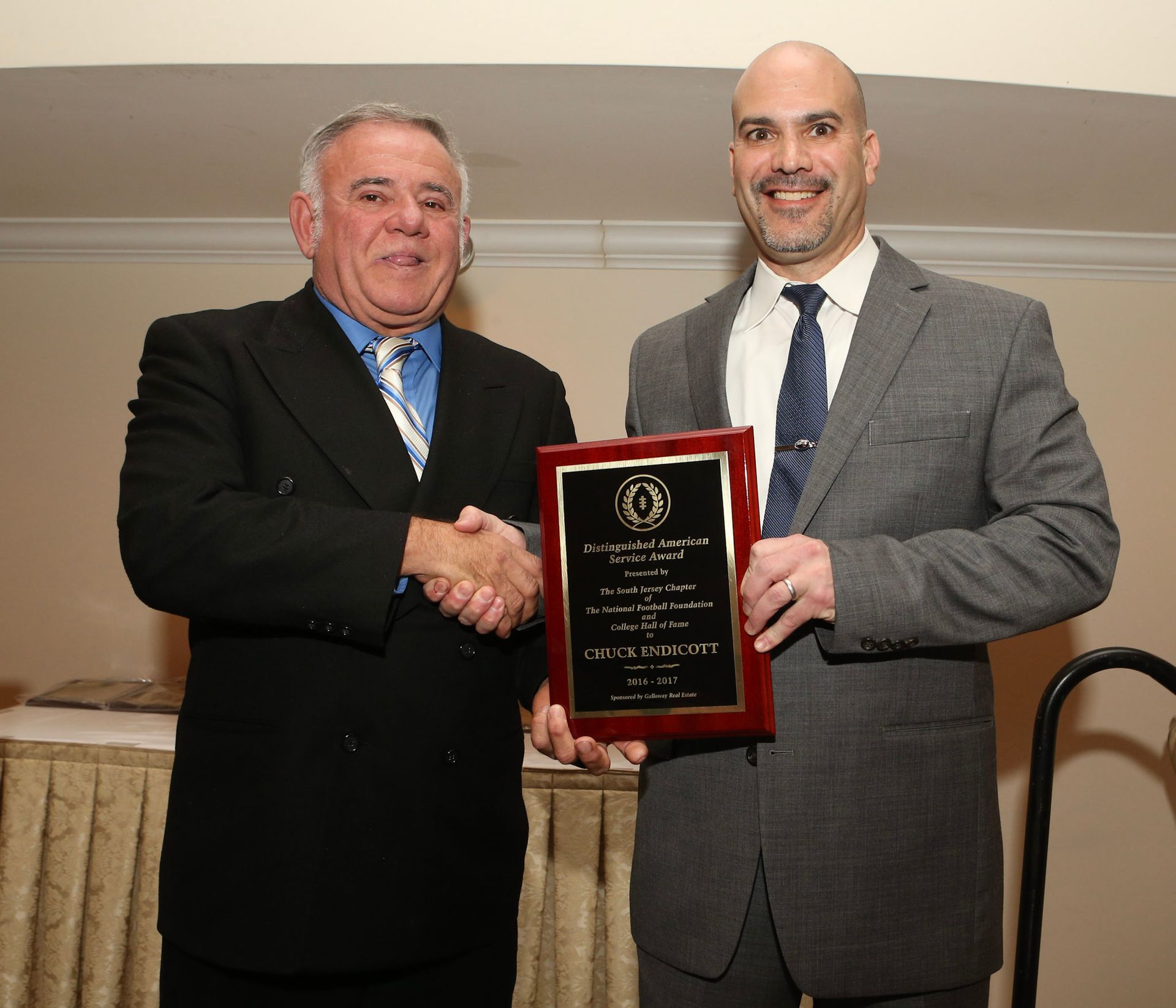 a man in a suit shakes hands with another man holding a plaque