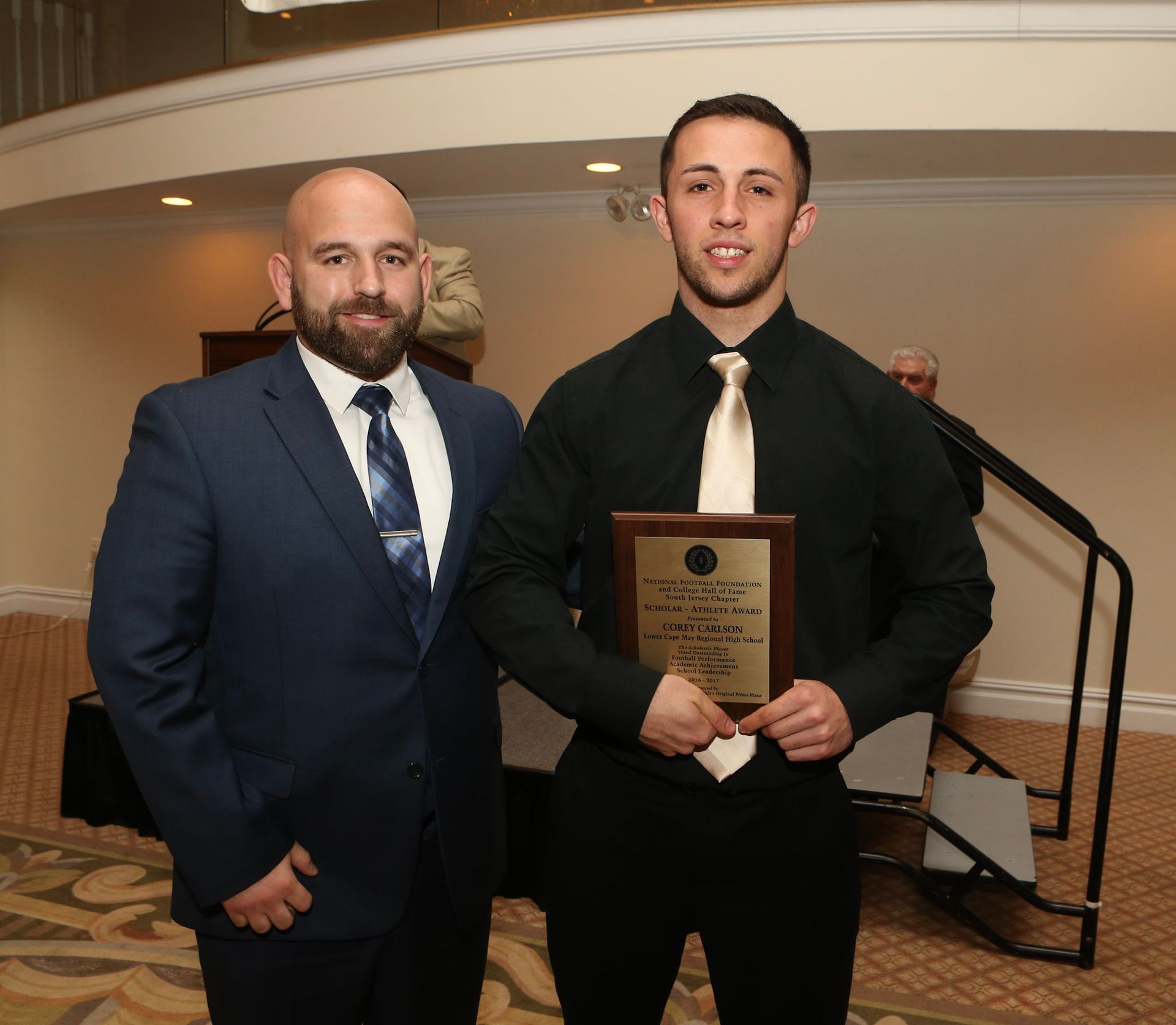 a man in a suit stands next to a man holding a plaque