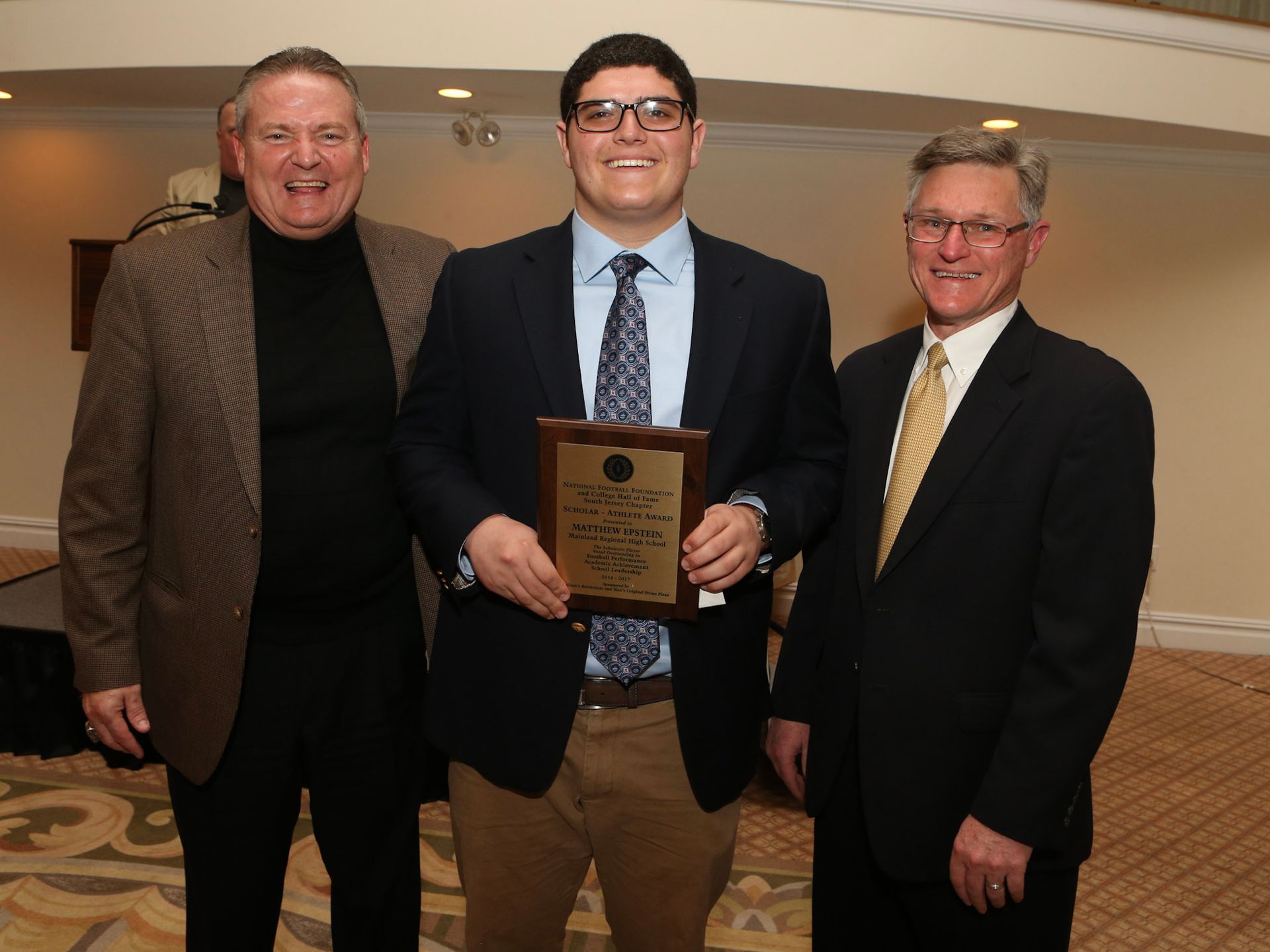three men are posing for a picture and one of them is holding a plaque