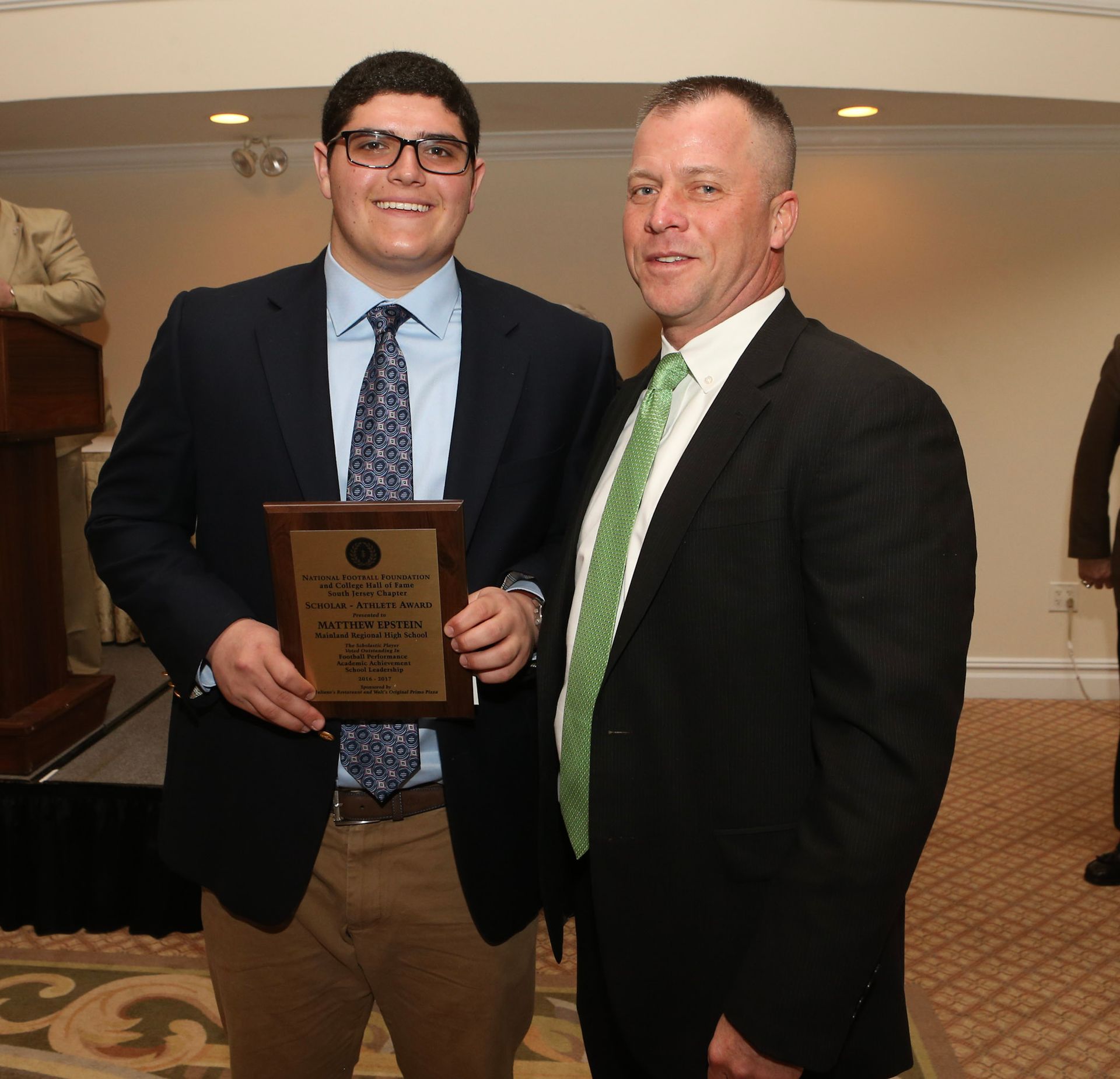 two men are posing for a picture and one is holding a plaque