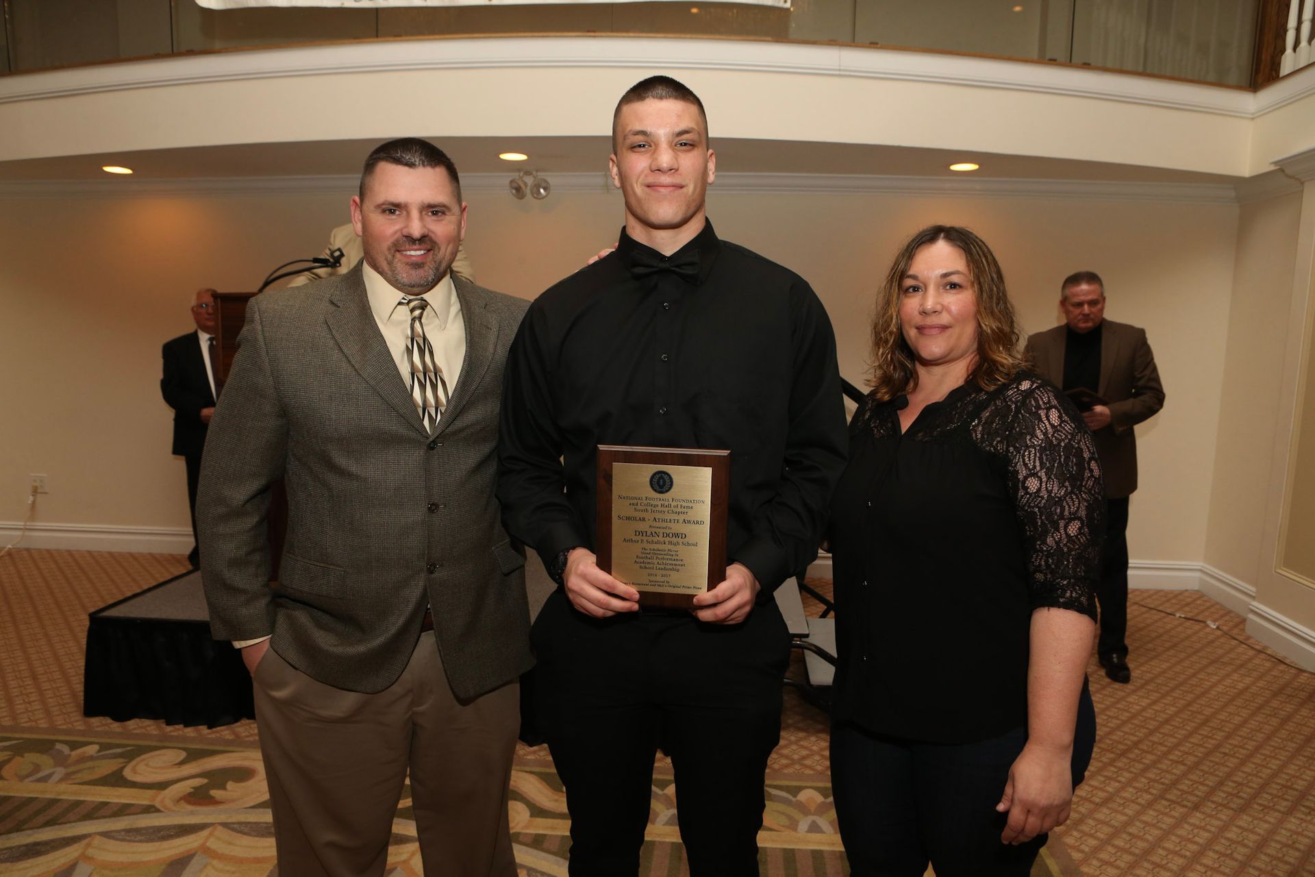 a man in a black shirt is holding a plaque while standing with two other people