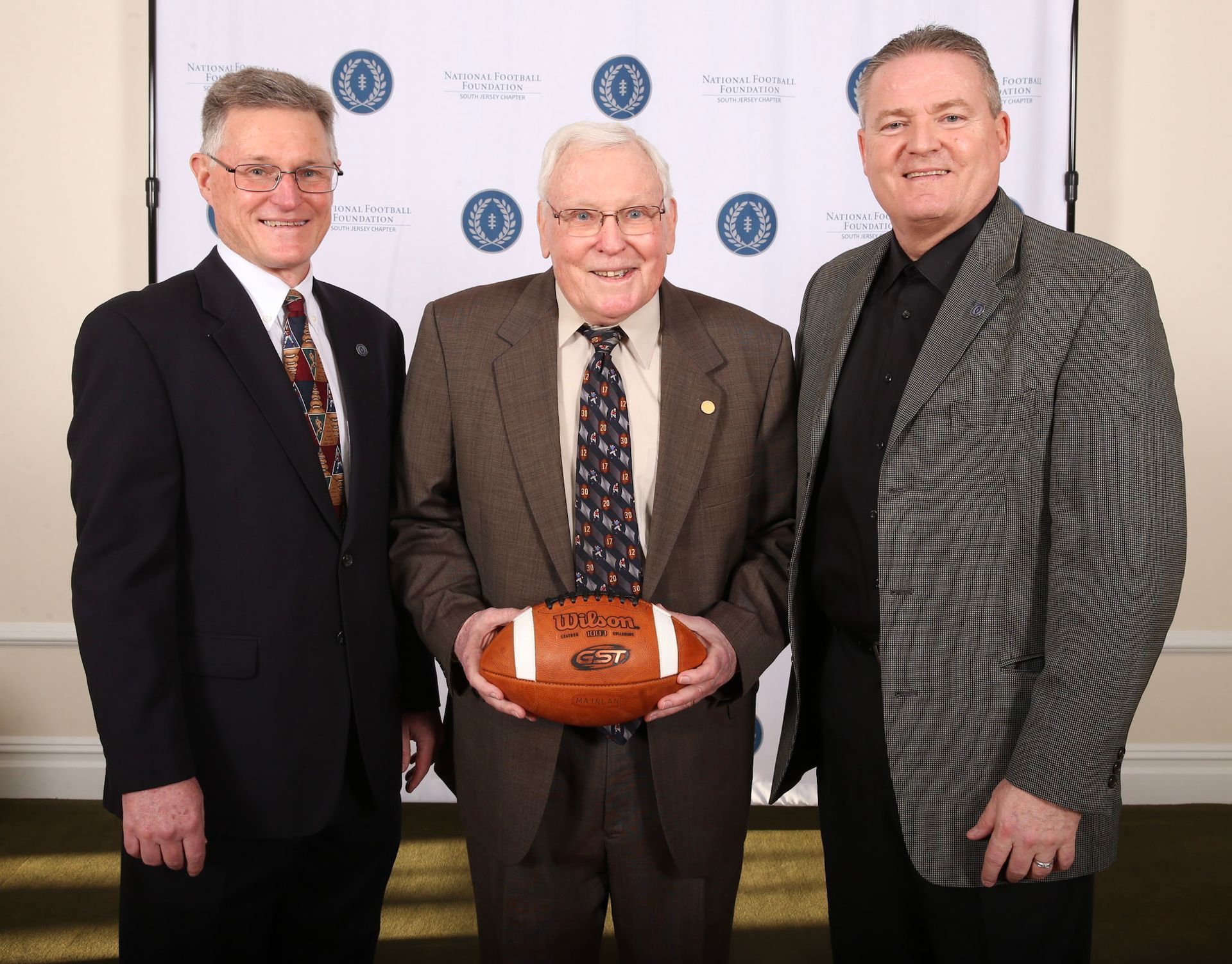 three men are posing for a picture and one of them is holding a football