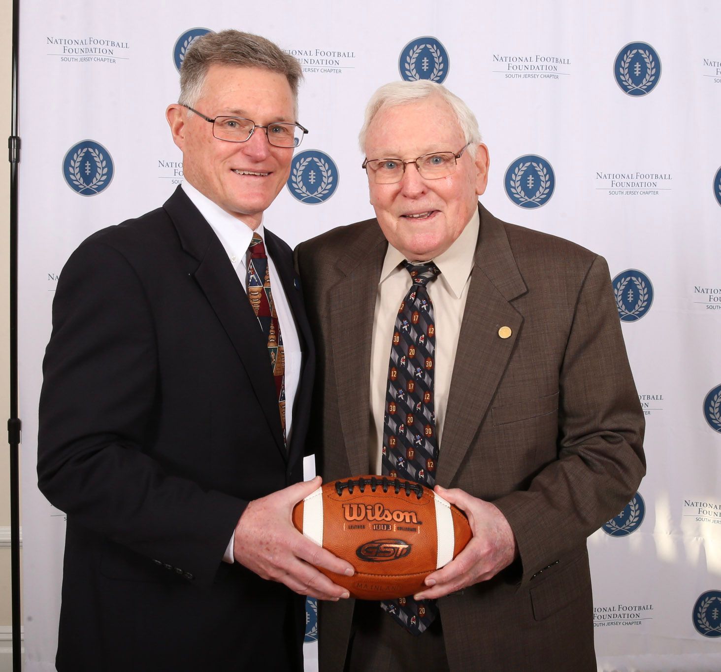 two men standing next to each other holding a wilson football