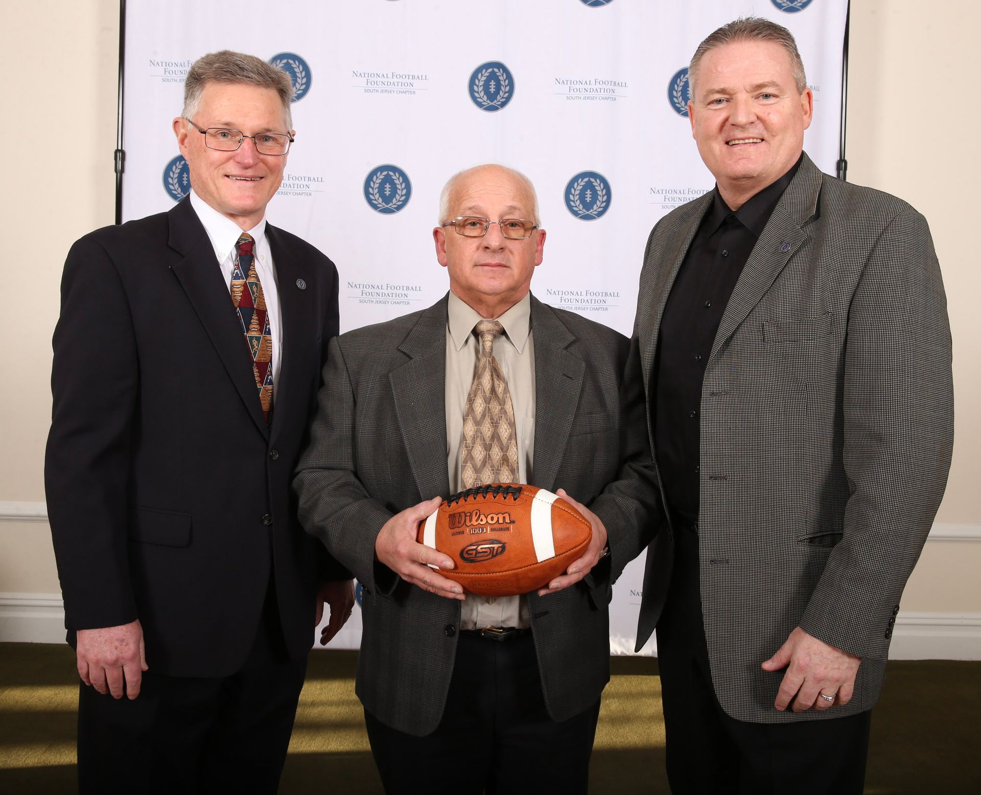 three men are posing for a picture and one of them is holding a football