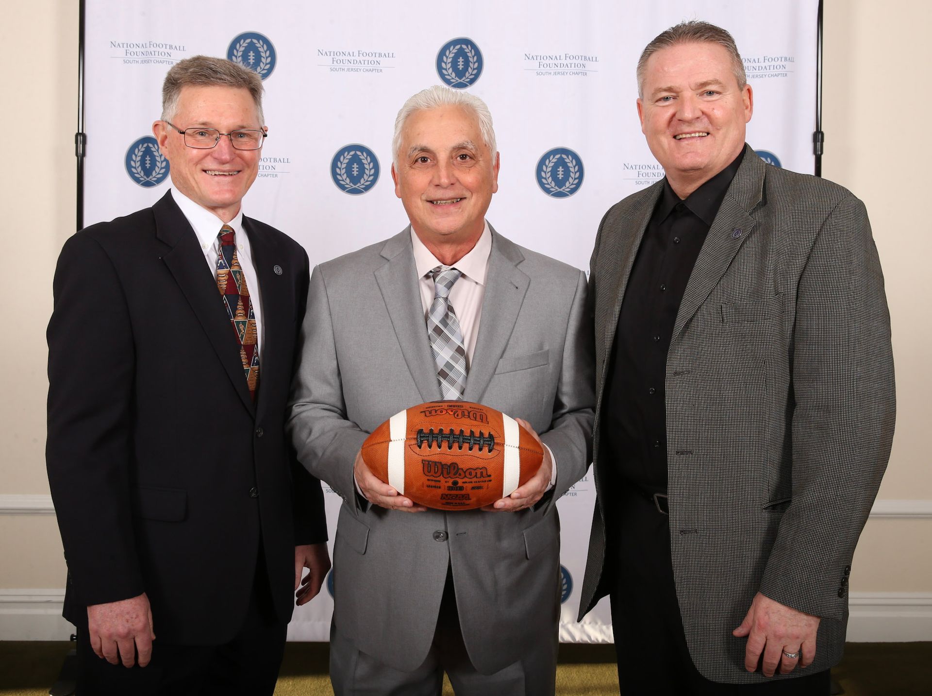 three men standing next to each other holding a wilson football