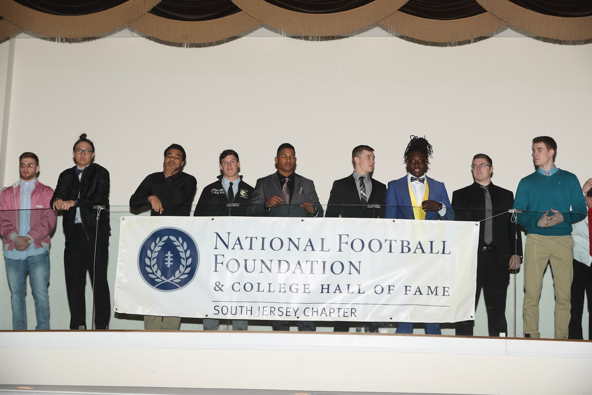 a group of men standing in front of a national football foundation banner