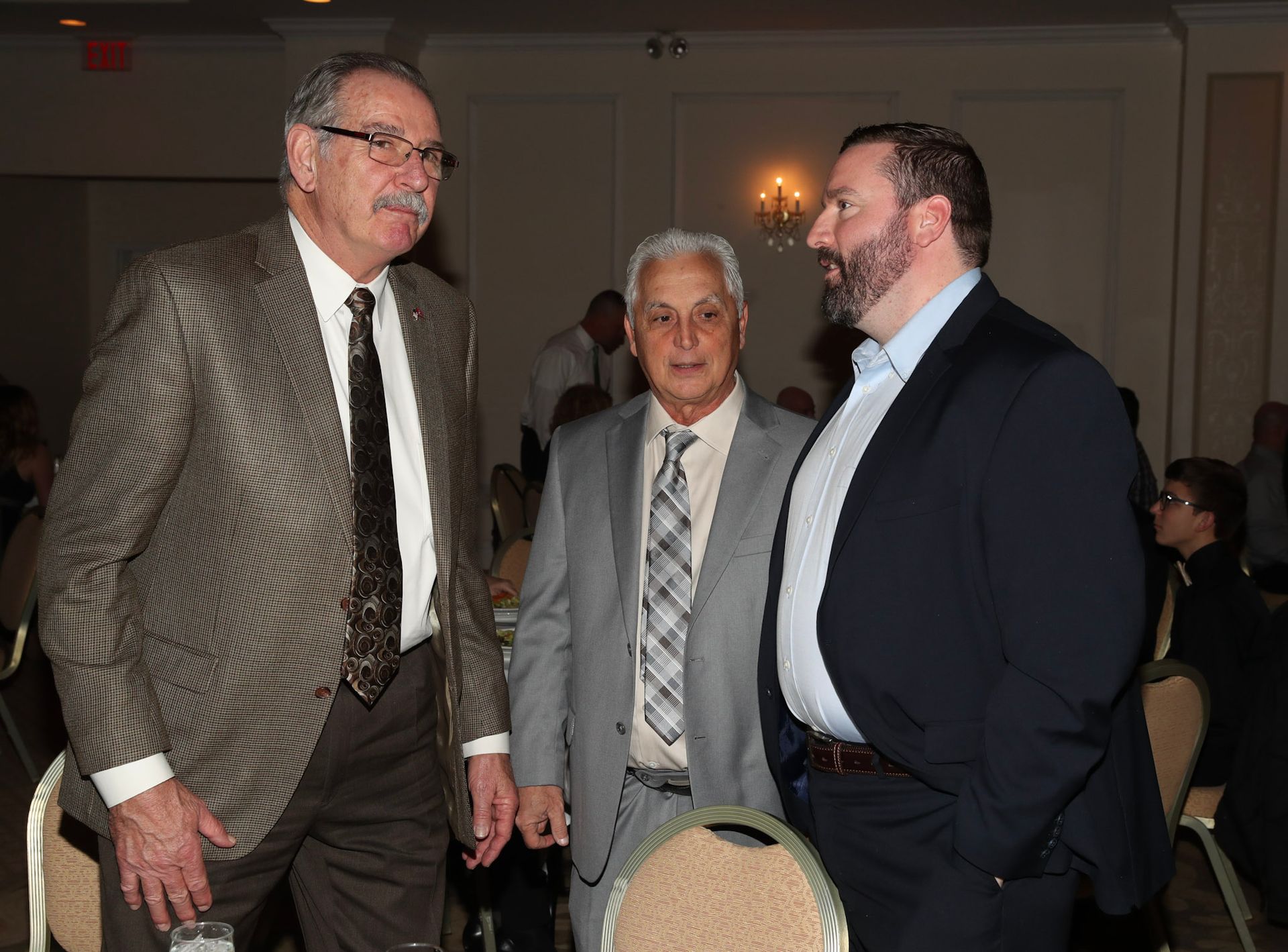 three men in suits and ties are talking in a room