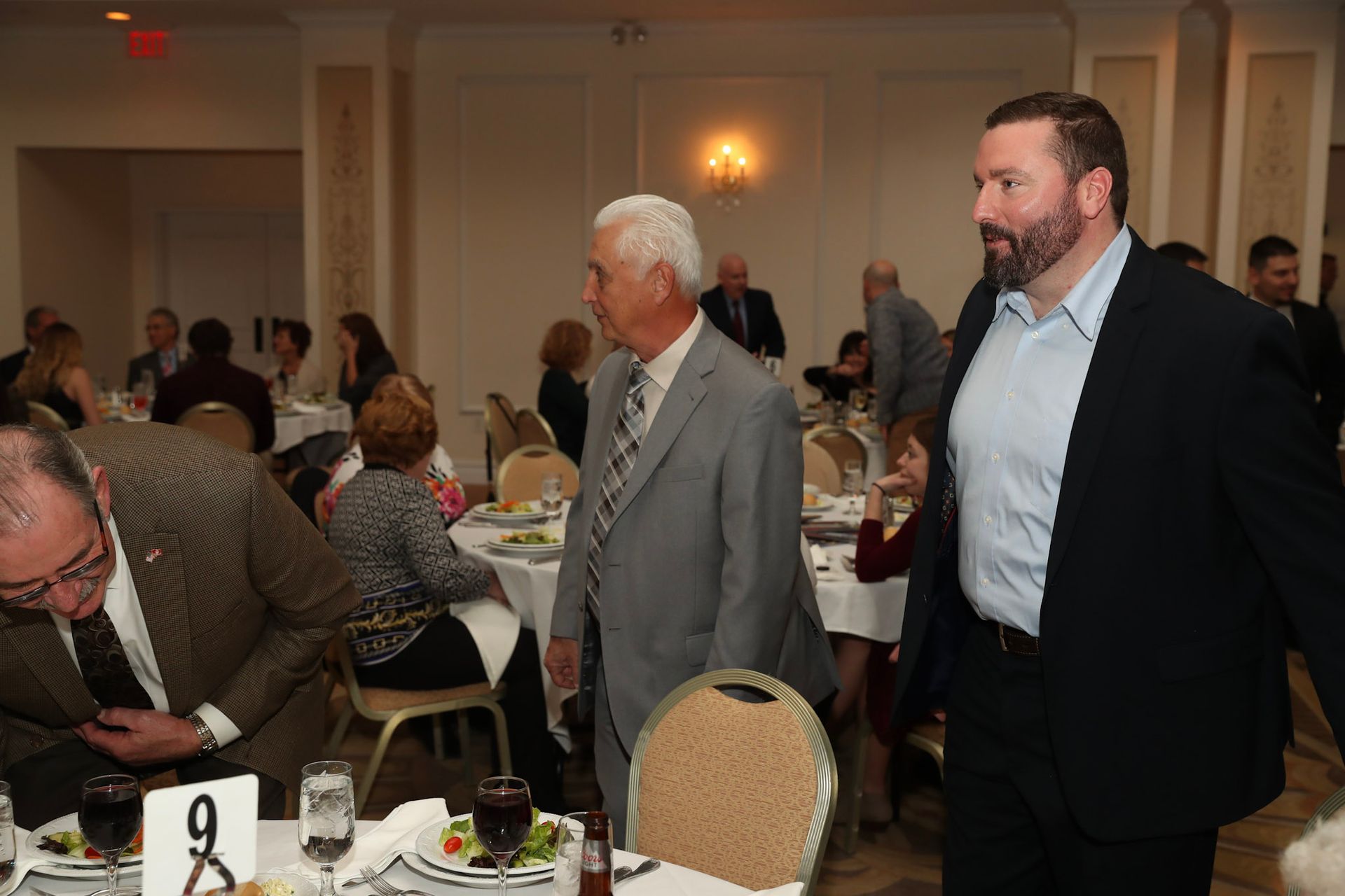a man in a suit walks past a table with a number 9 on it