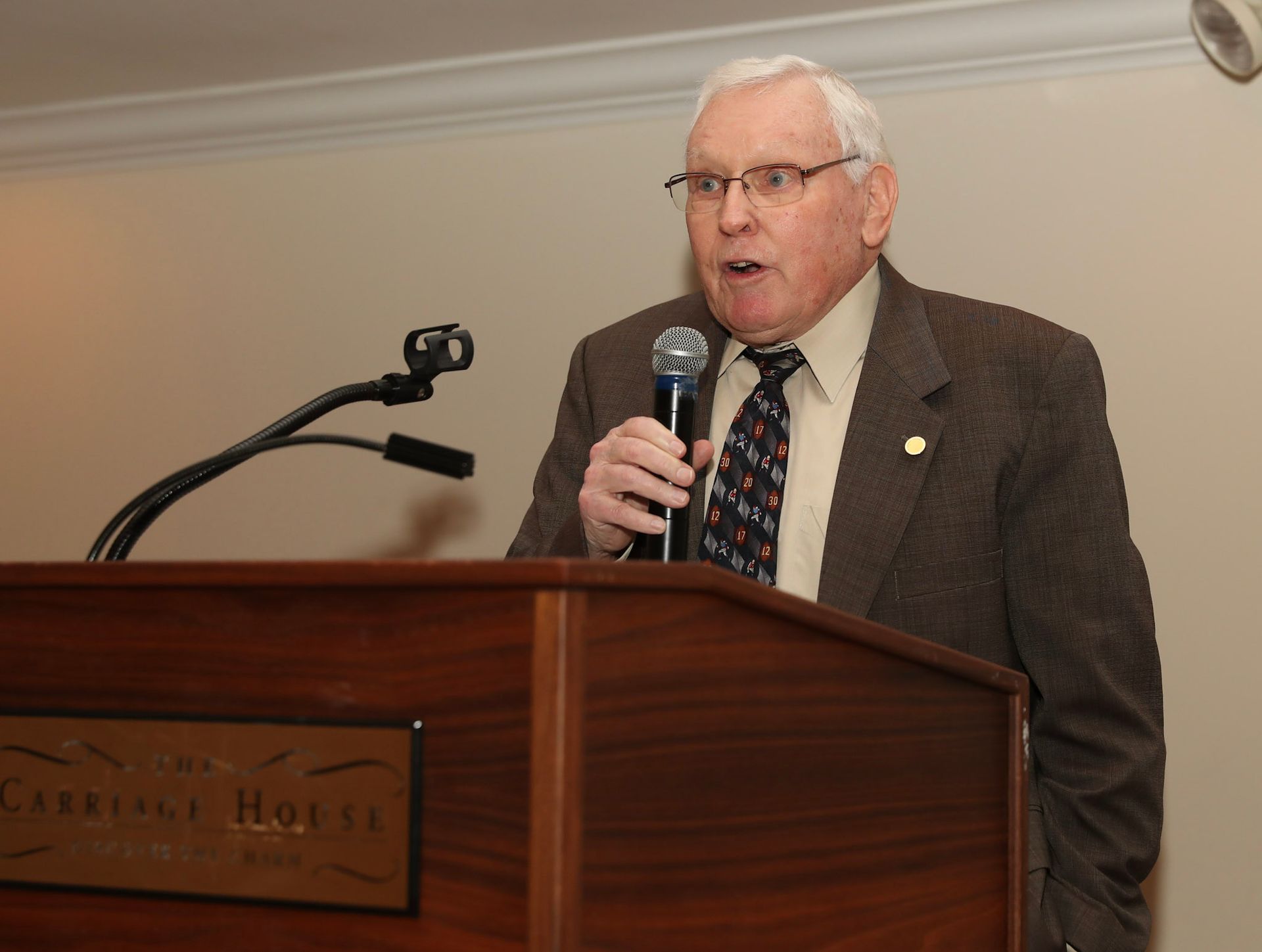 a man stands at a podium holding a microphone in front of a sign that says charles hotel