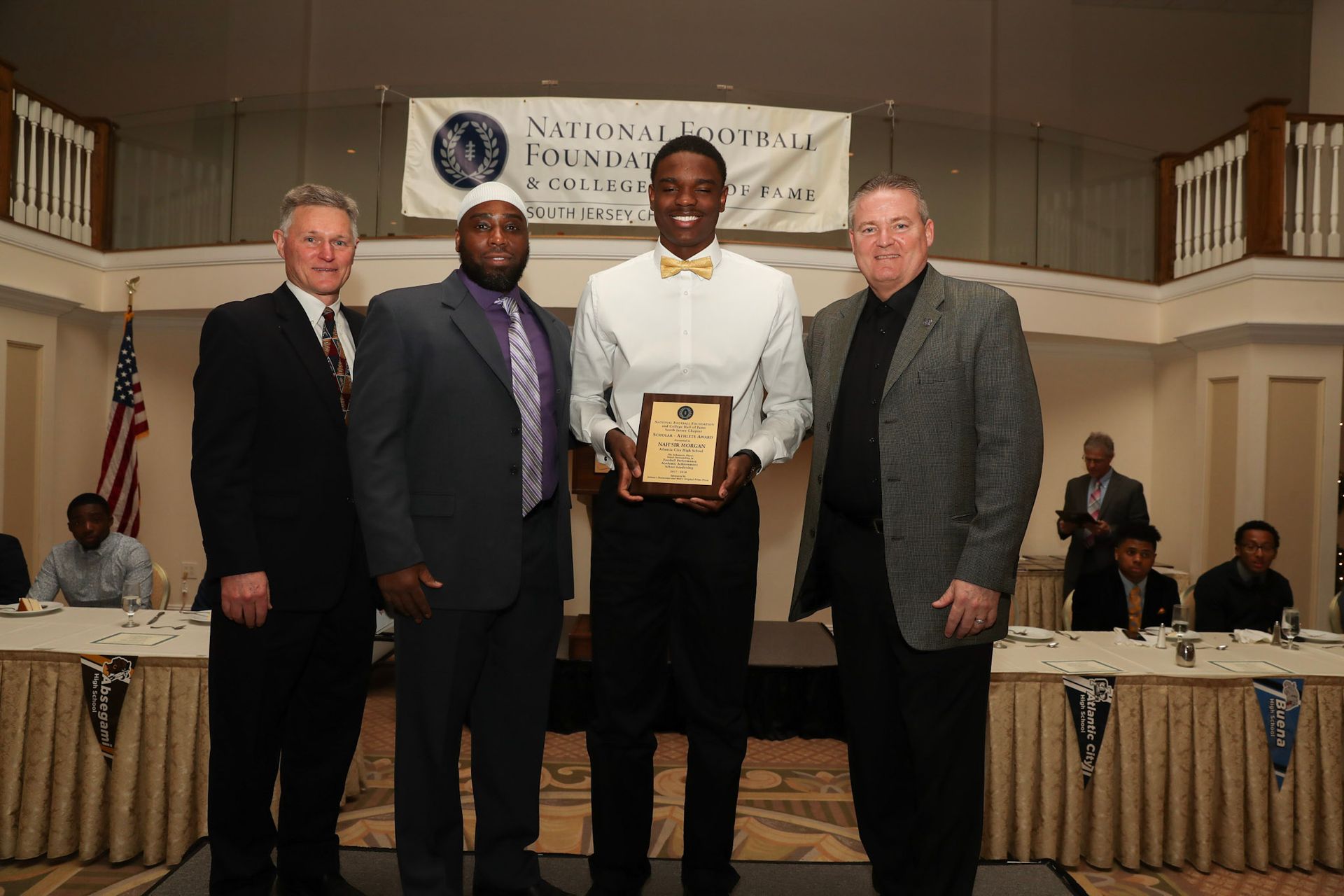 a man in a bow tie holds a plaque in front of a group of men
