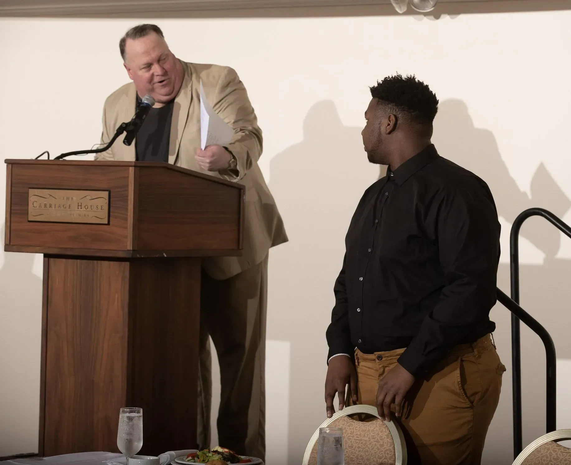 a man stands at a podium with a microphone while another man looks on