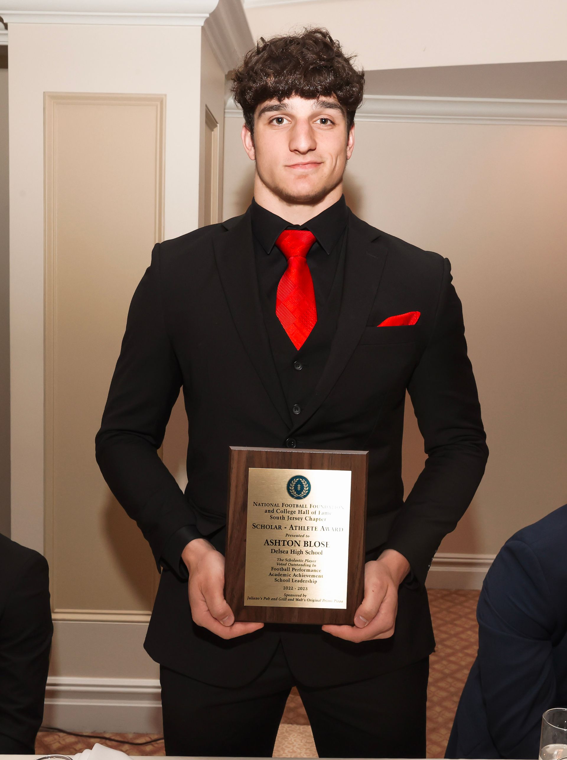 a man in a black suit and red tie is holding a plaque