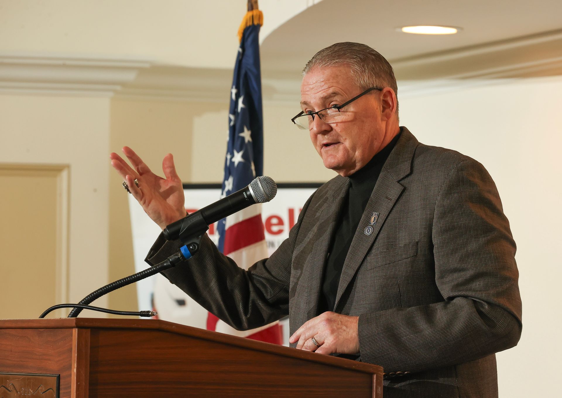 Mike Gately stands at a podium speaking into a microphone