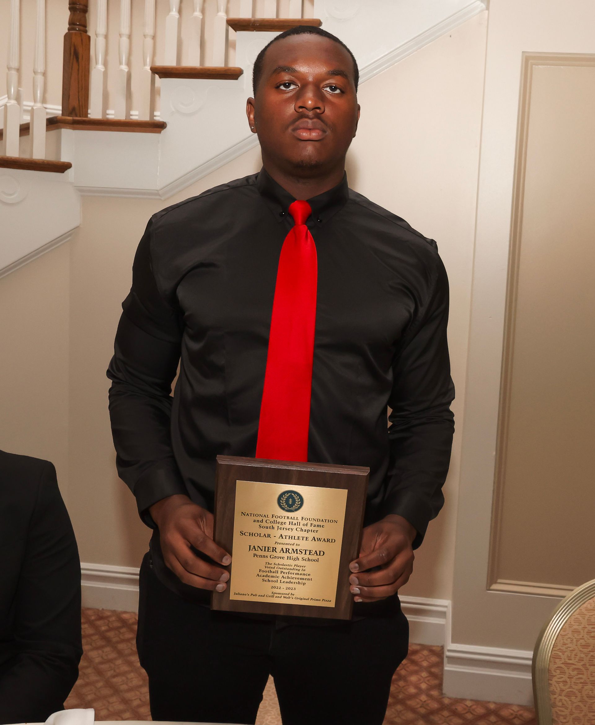 a man in a black shirt and red tie is holding a plaque