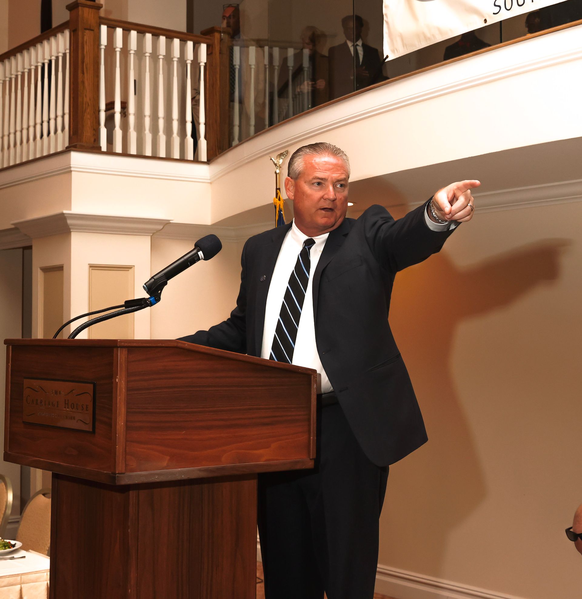 a man in a suit and tie stands at a podium pointing