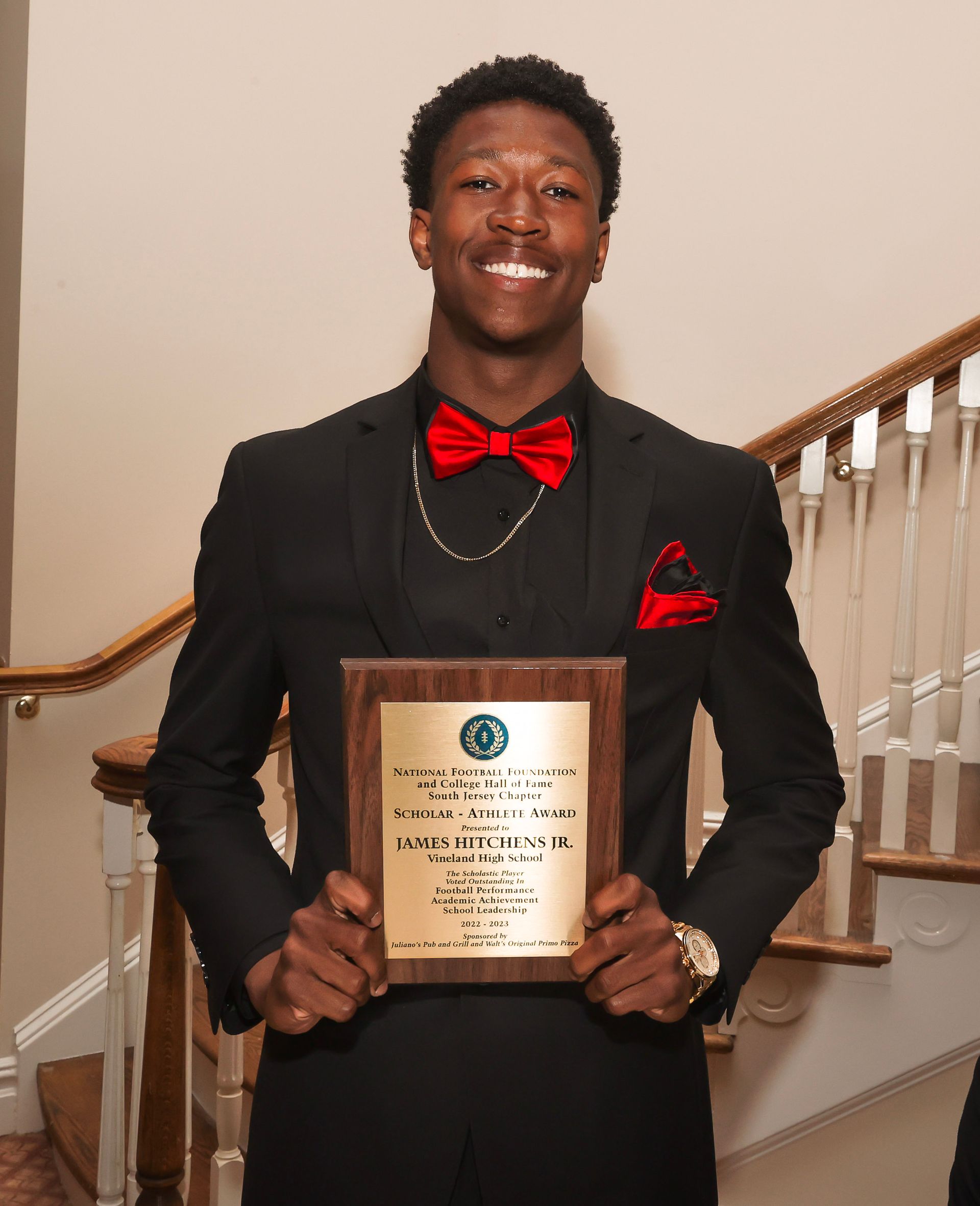 a man in a black suit and red bow tie is holding a plaque