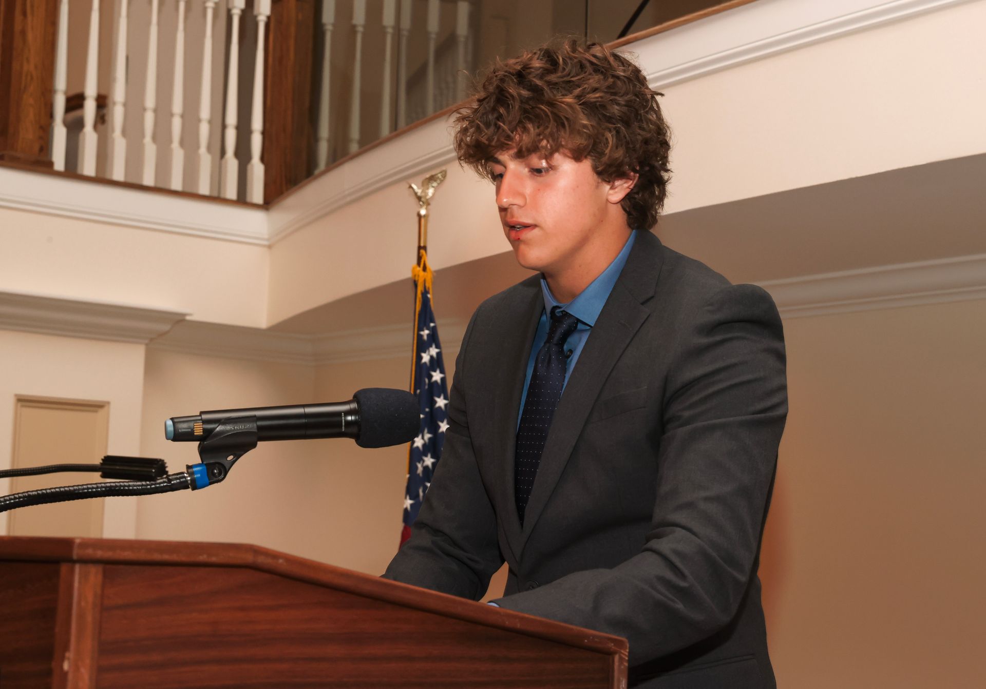 a young man in a suit and tie stands at a podium speaking into a microphone