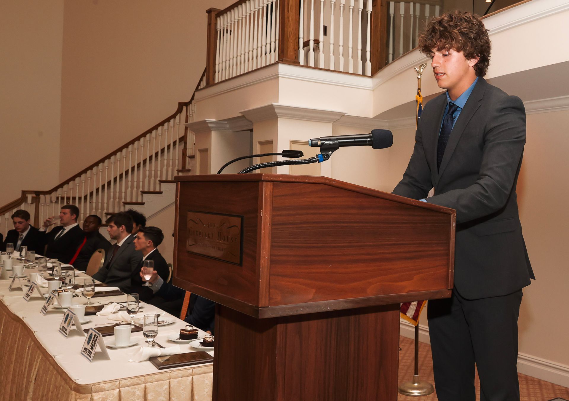 a man in a suit stands at a podium giving a speech
