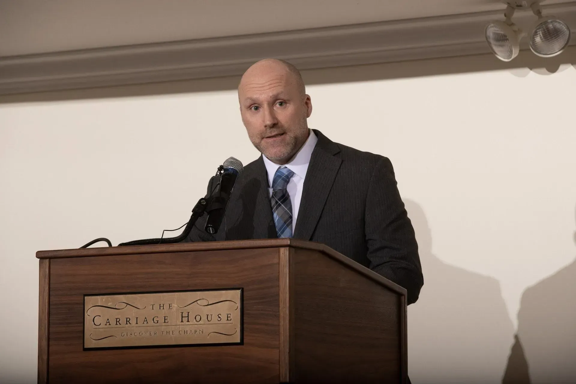 a bald man in a suit and tie stands at a podium with a microphone