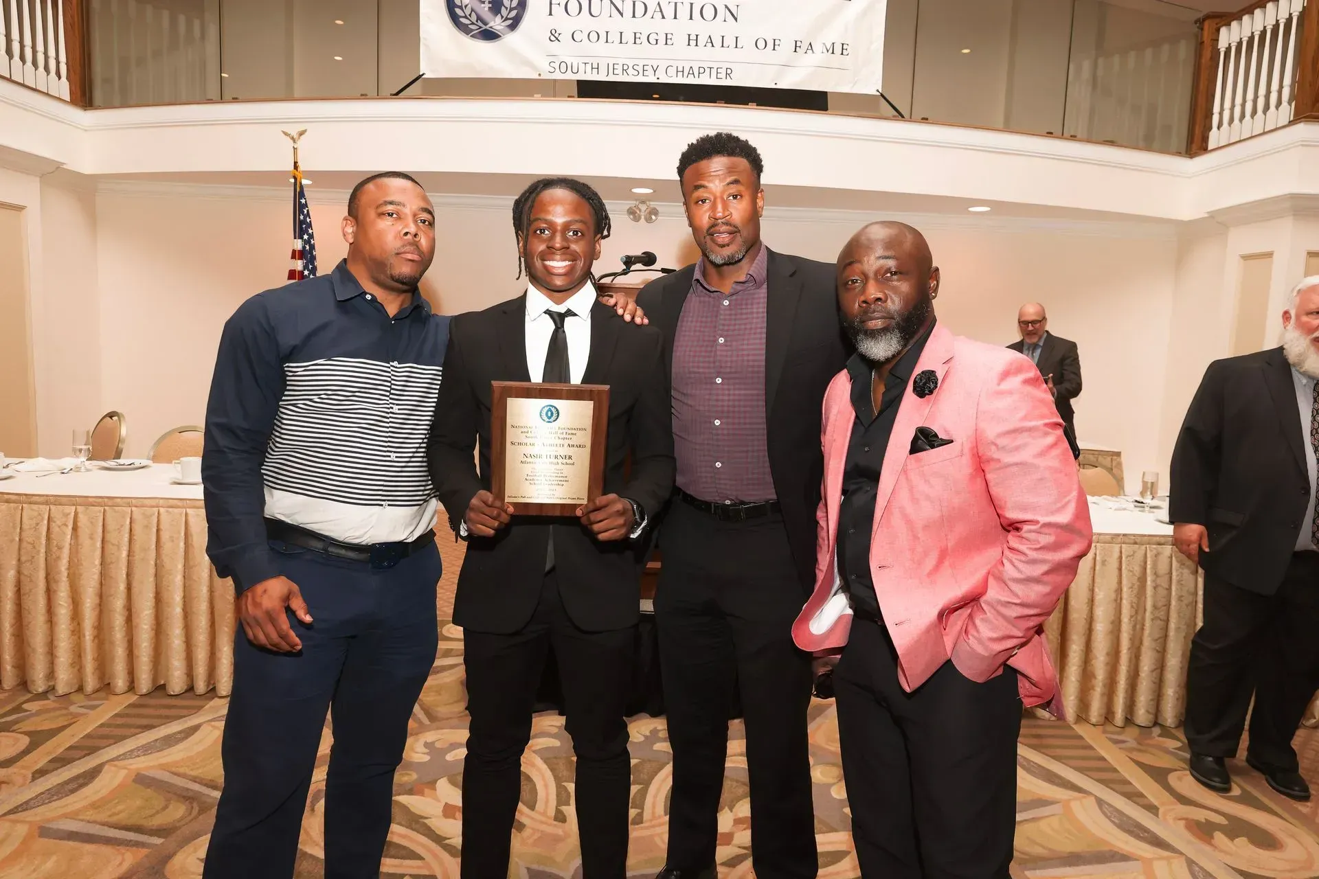 a man in a pink jacket holds a plaque with the letter d on it