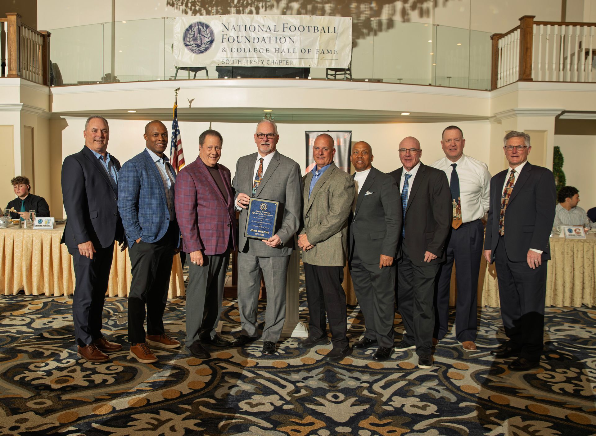 A group of men in suits pose for a photo on a stage holding an award during a National Football Foundation event
