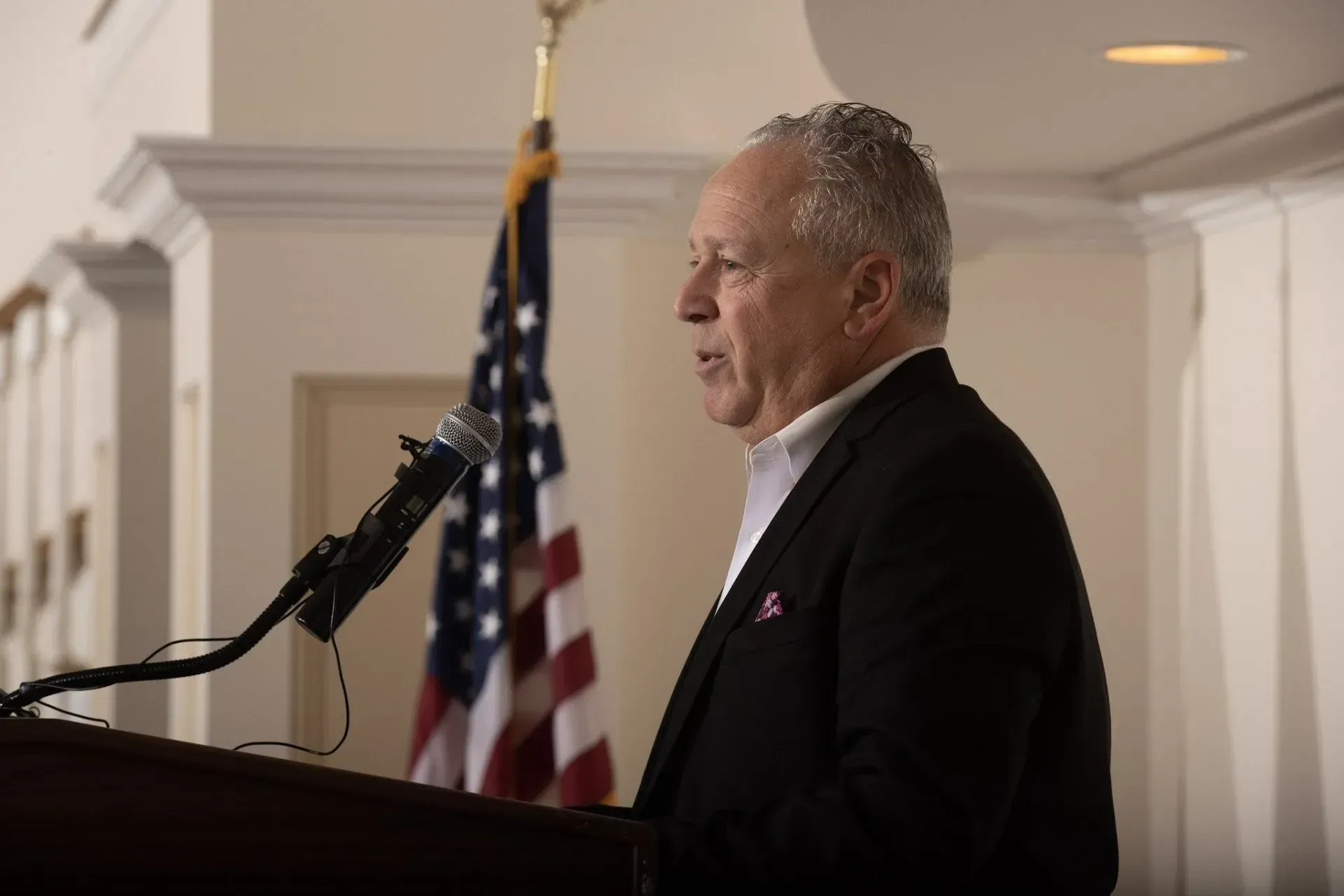 a man in a suit is giving a speech at a podium in front of an american flag .