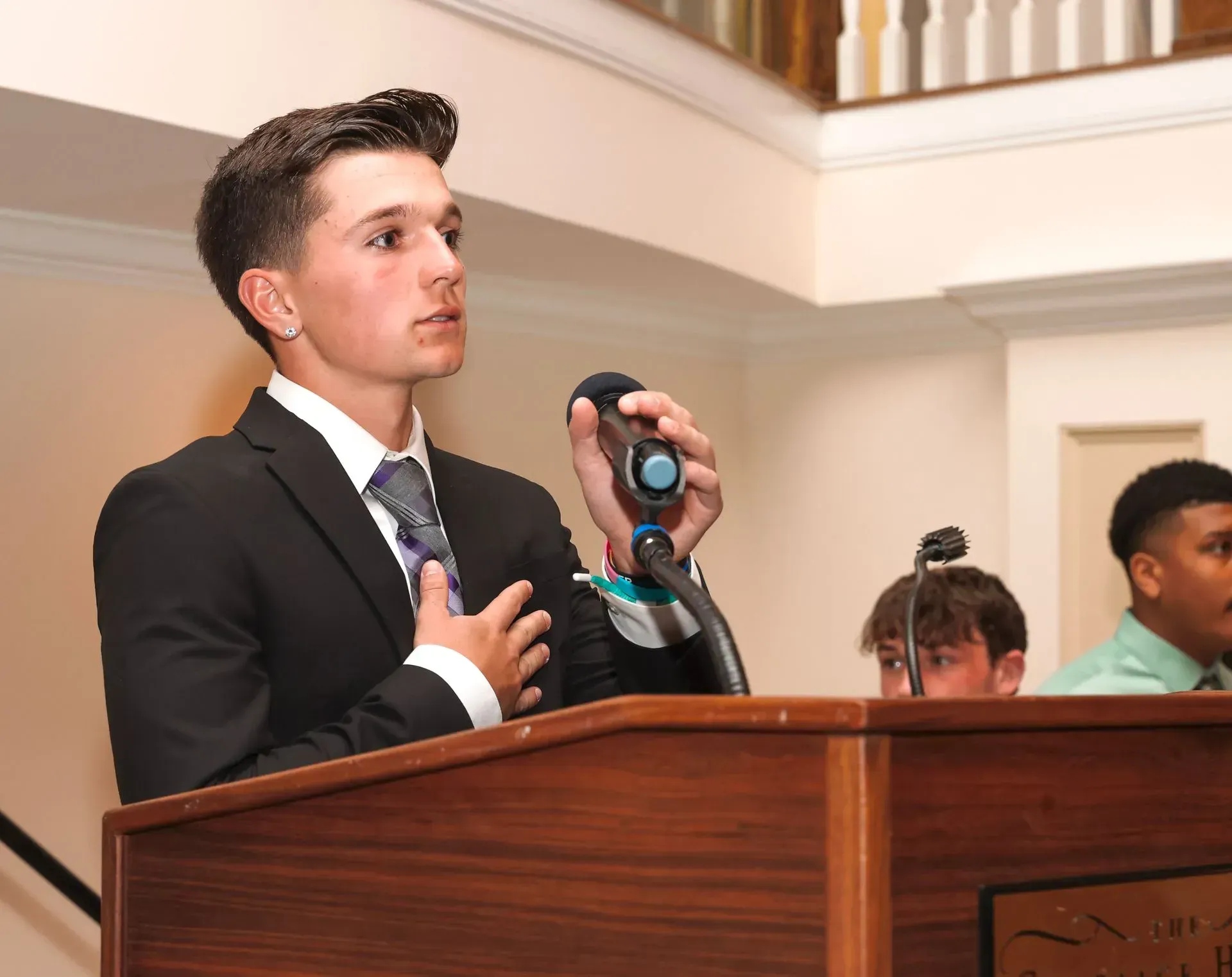 a man in a suit and tie stands at a podium holding a microphone