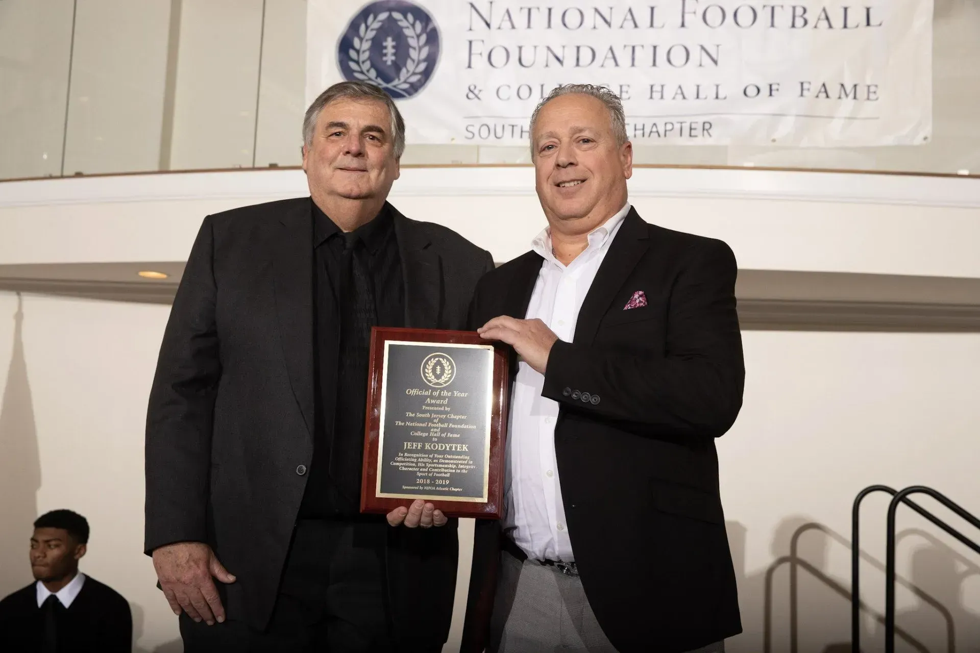 two men are standing in front of a national football foundation banner