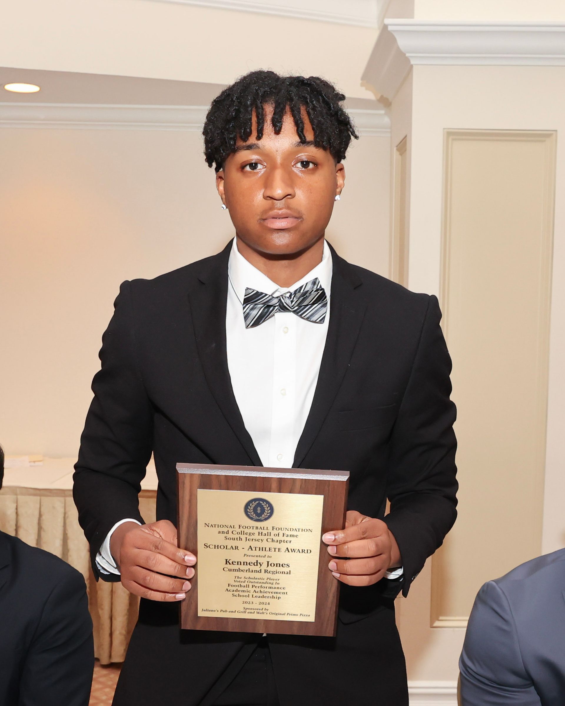 A man in a suit and bow tie is holding a plaque