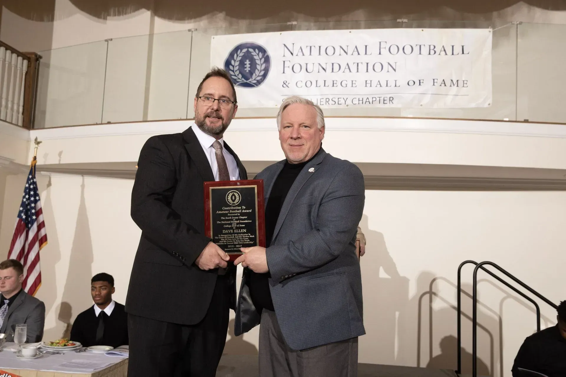 two men standing in front of a national football foundation banner