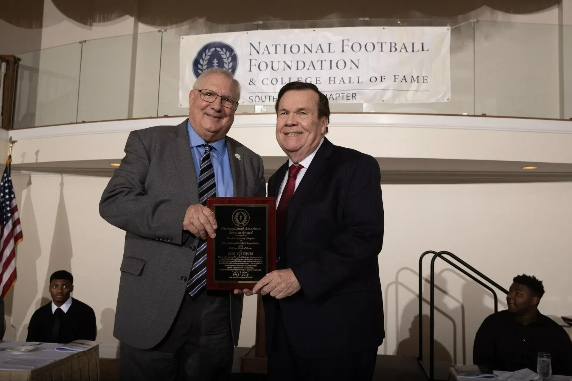 two men standing in front of a national football foundation banner