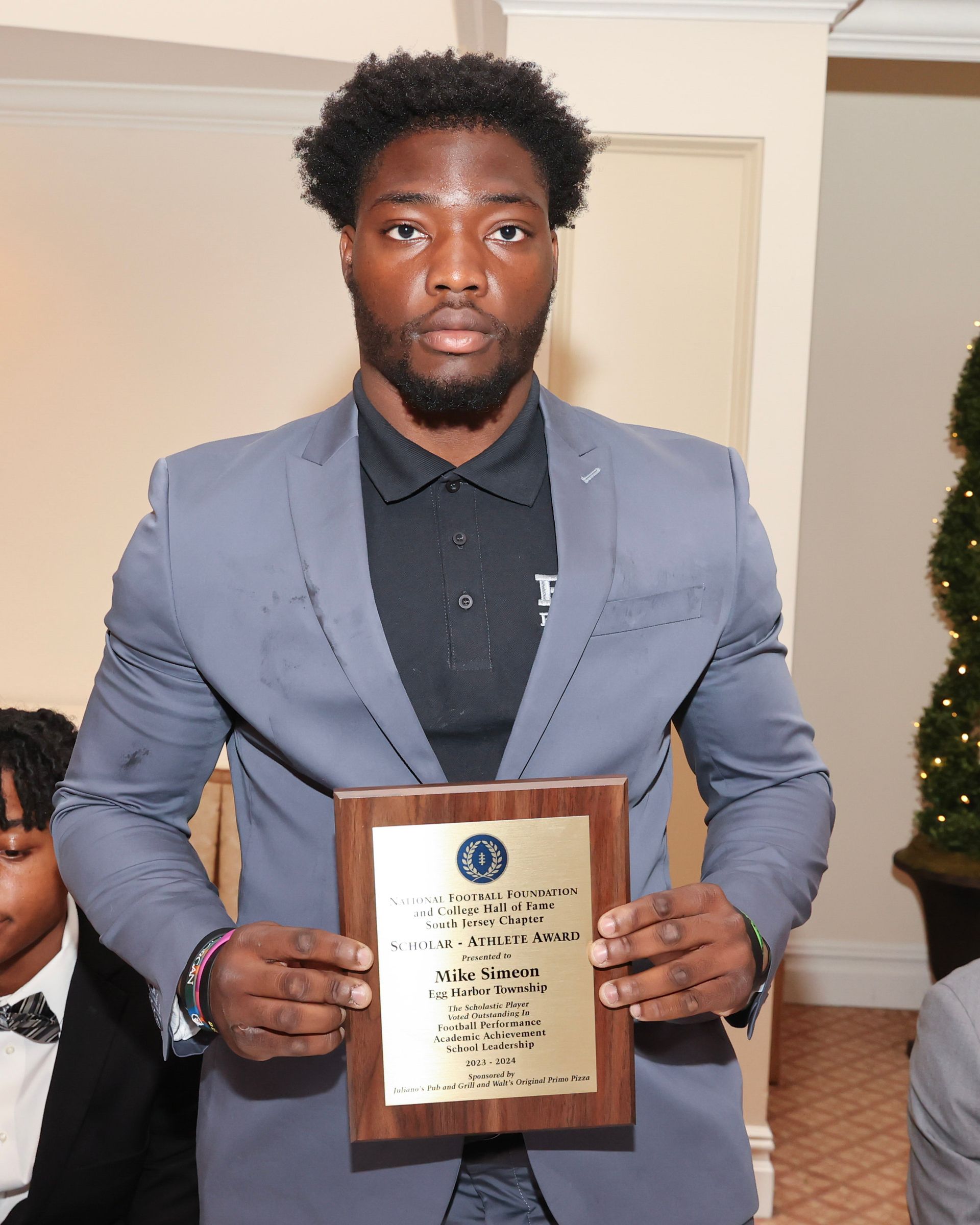 A man in a suit is holding a wooden plaque