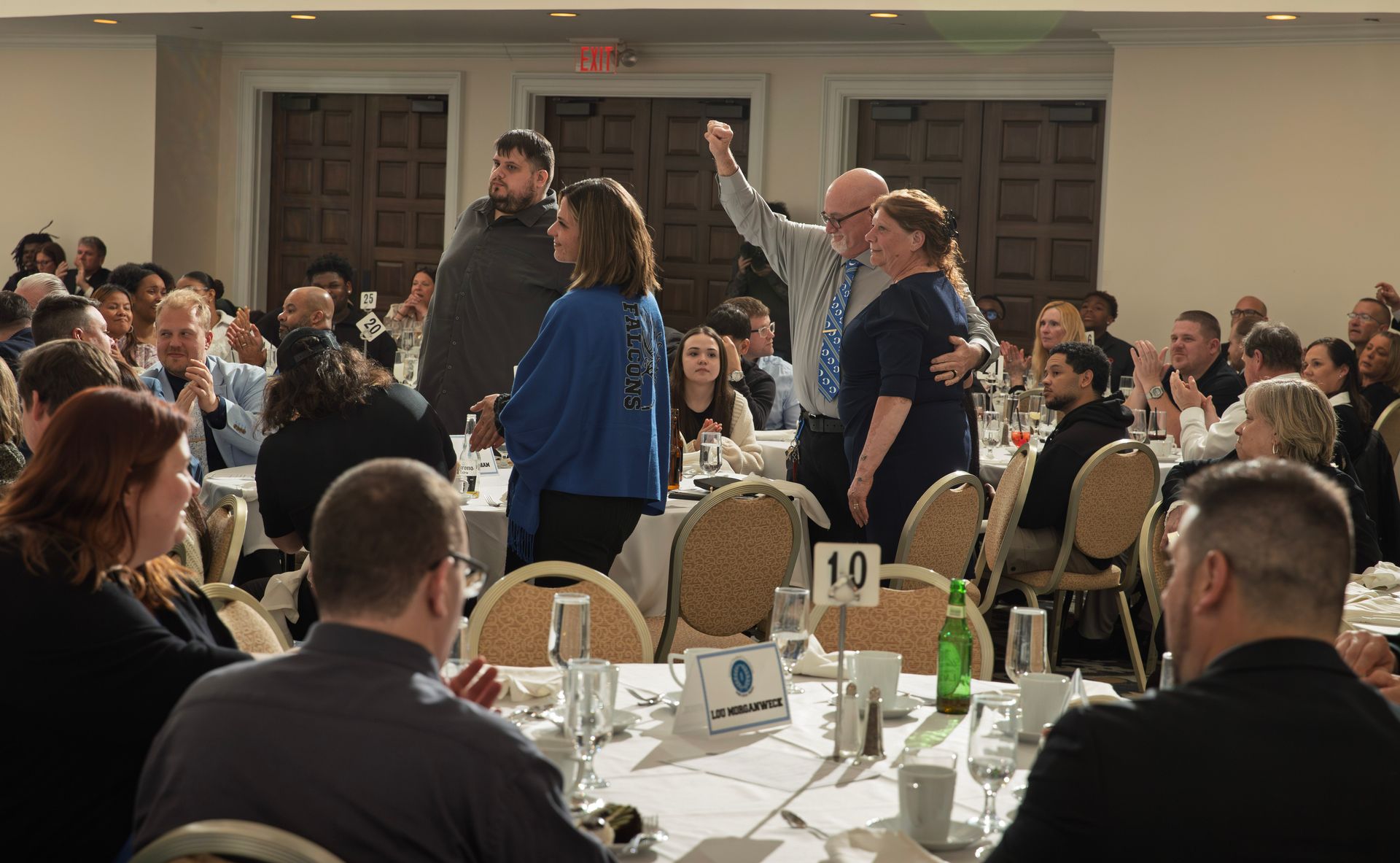 People at tables in a conference hall with one person standing and raising their arm in celebration
