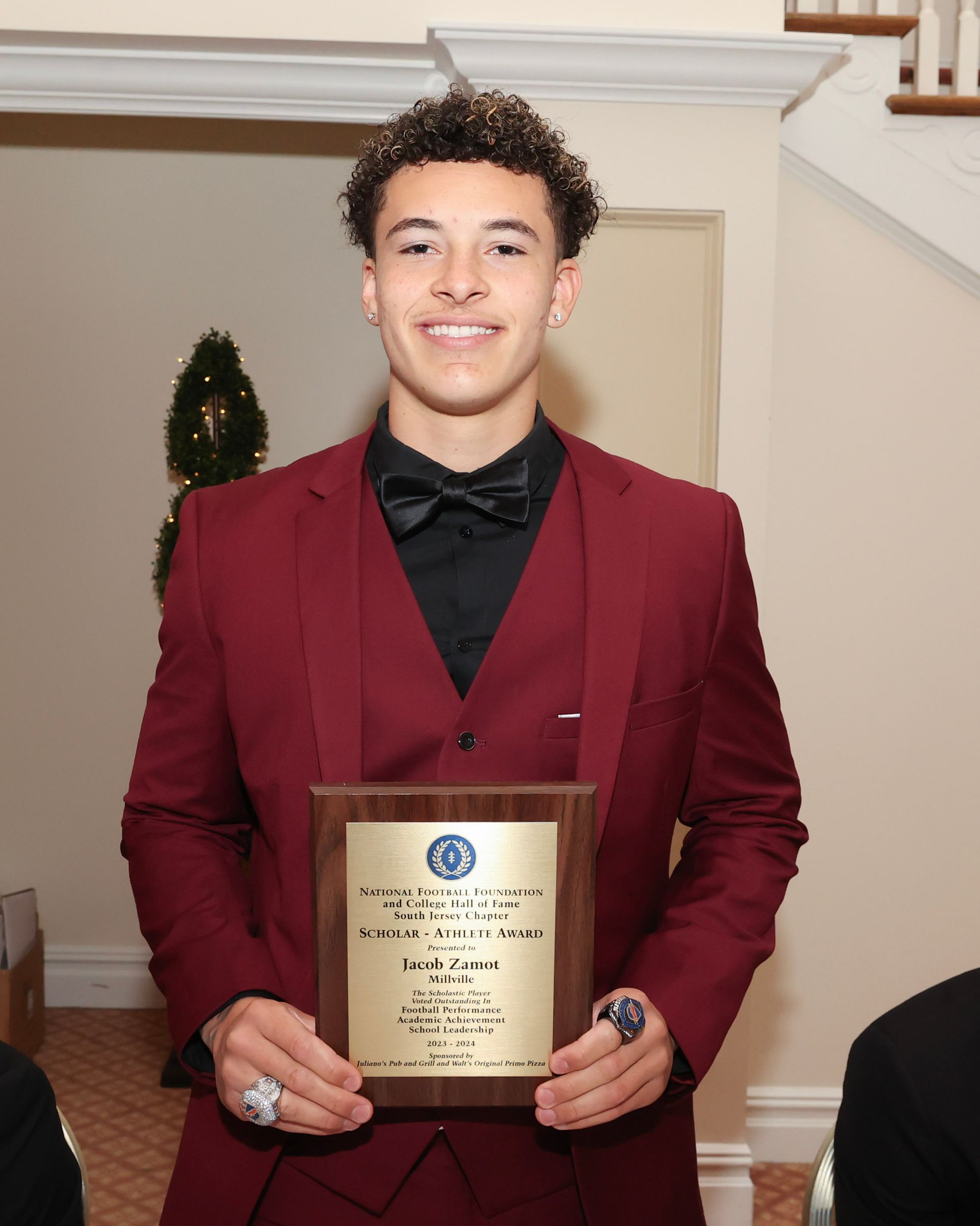 A young man in a red suit is holding a plaque