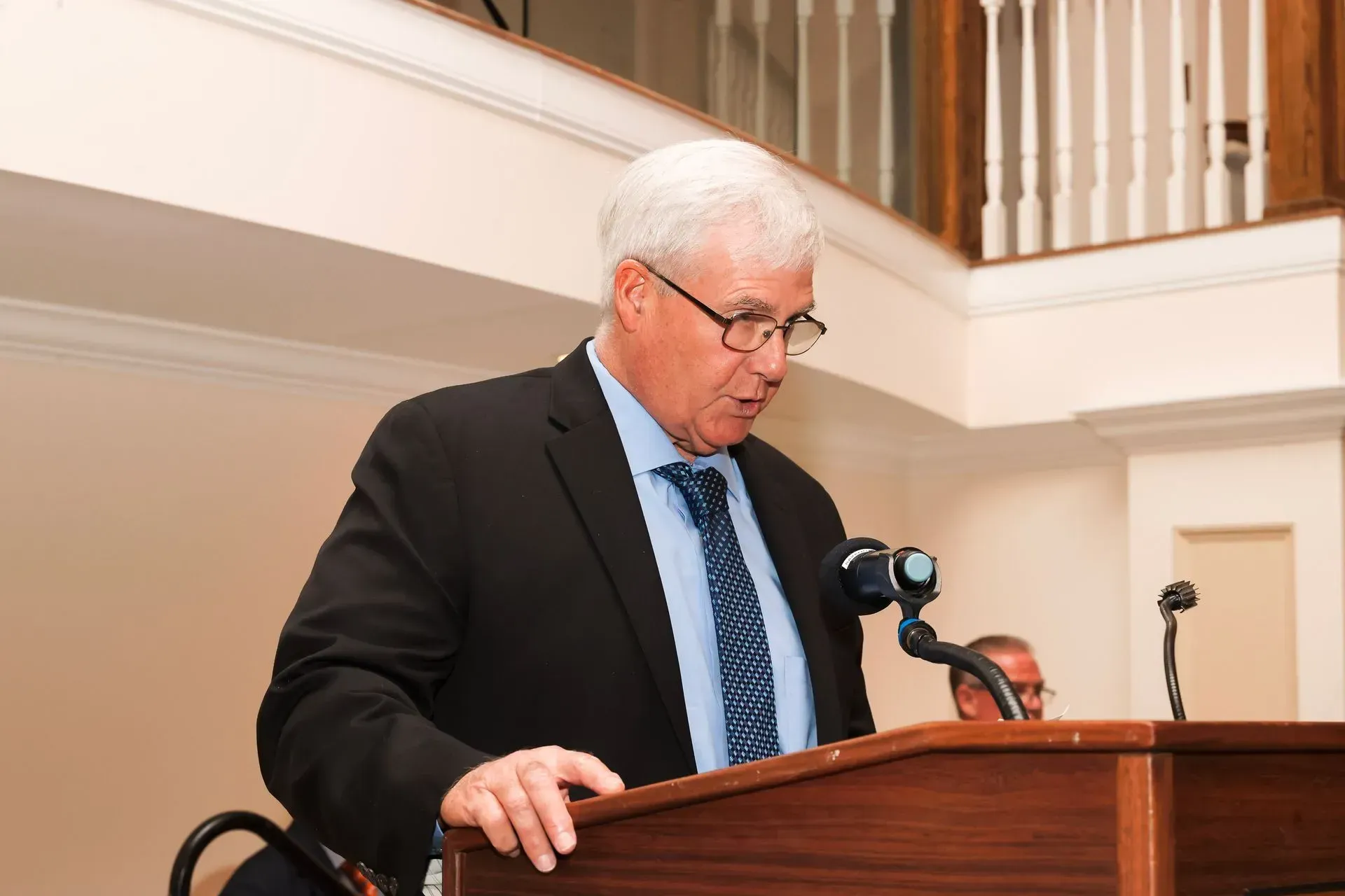 a man in a suit and tie stands at a podium speaking into a microphone