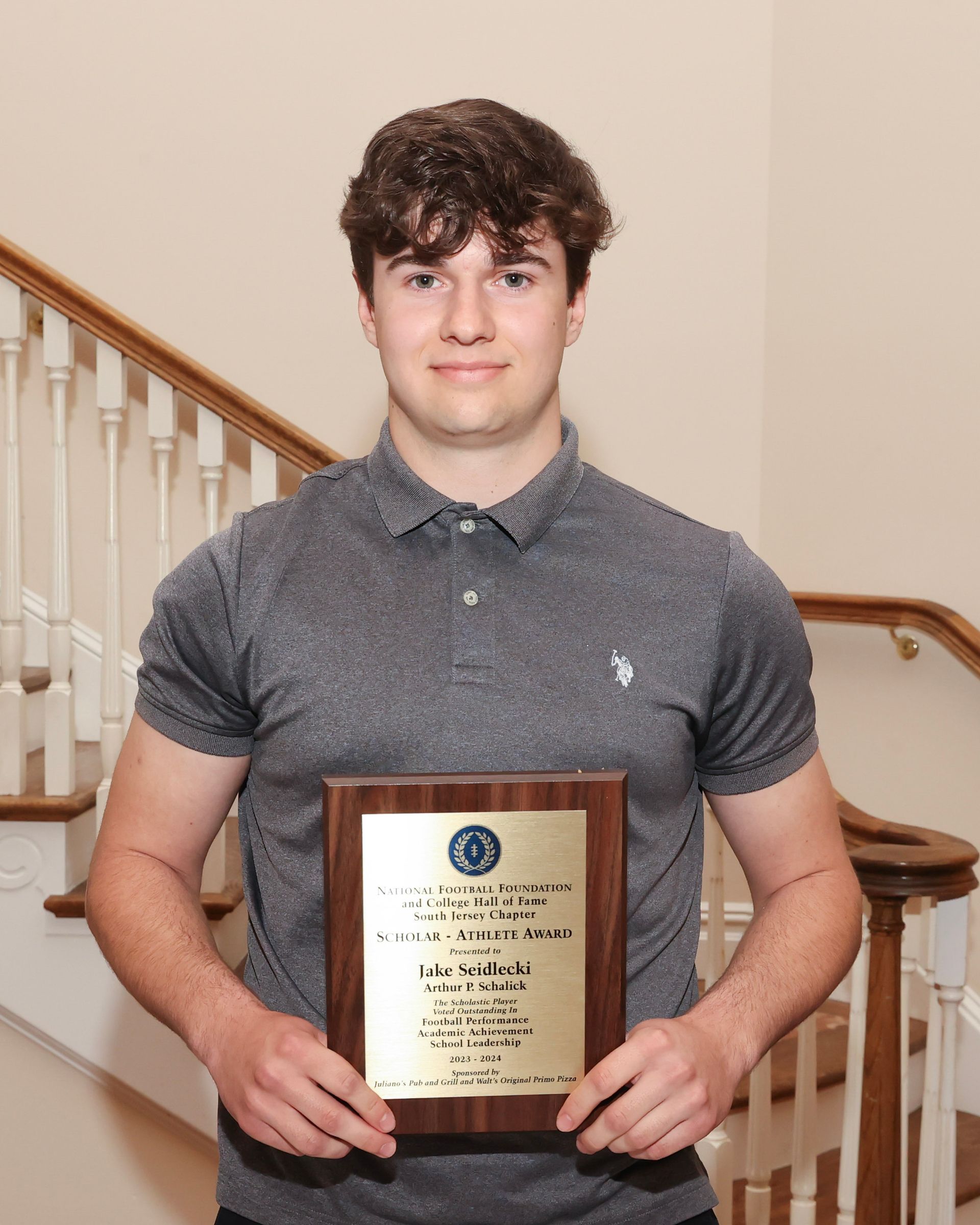 A young man is holding a plaque in front of a staircase