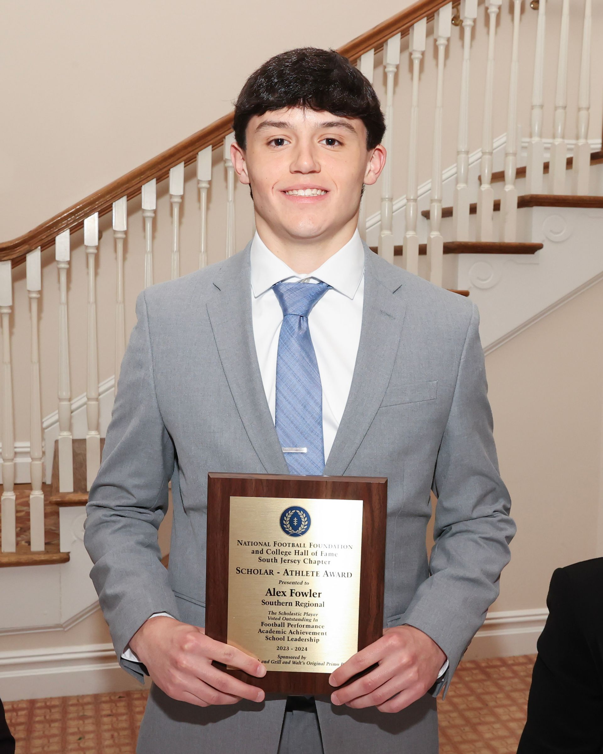 A young man in a suit and tie is holding a plaque