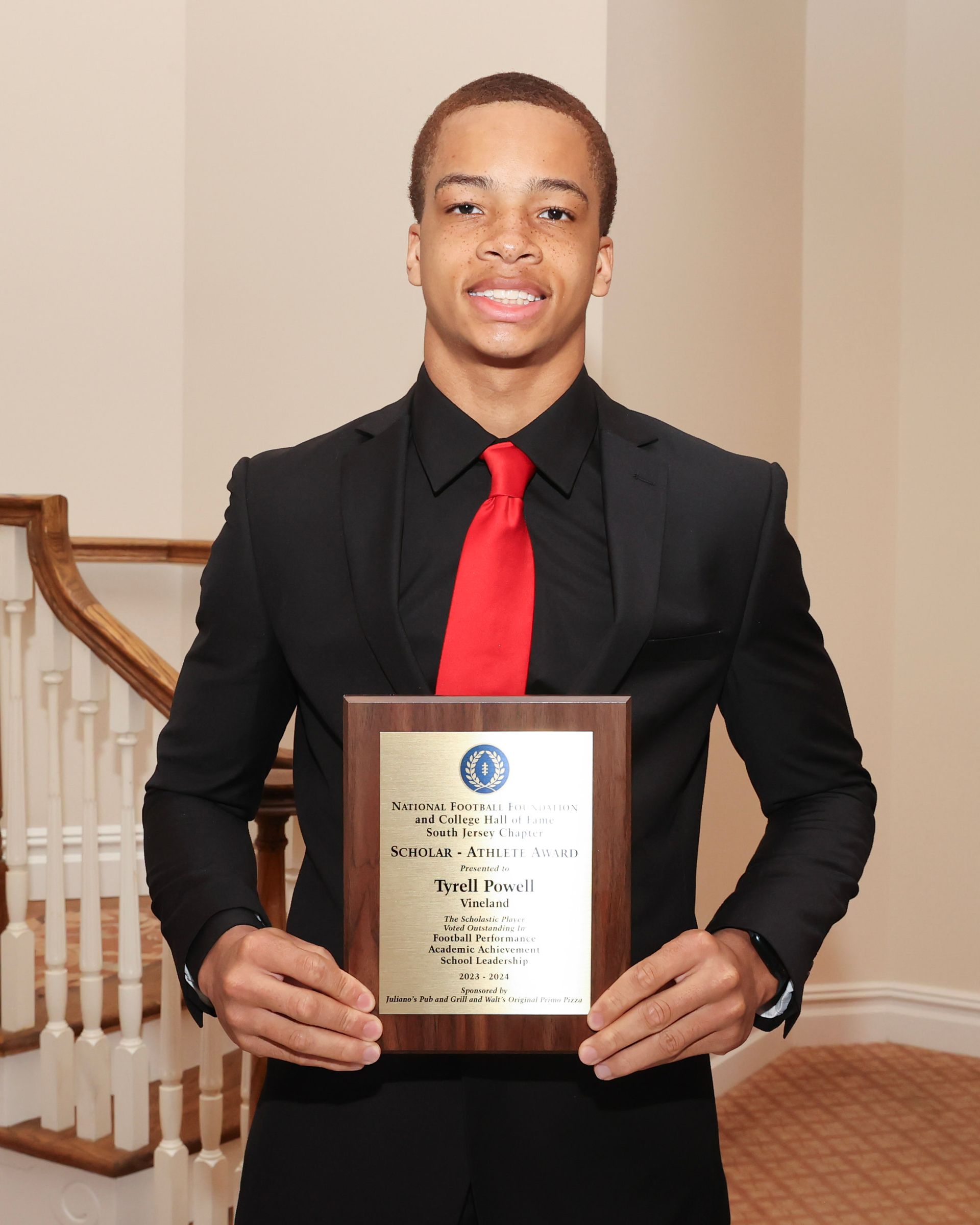 A man in a suit and red tie is holding a plaque