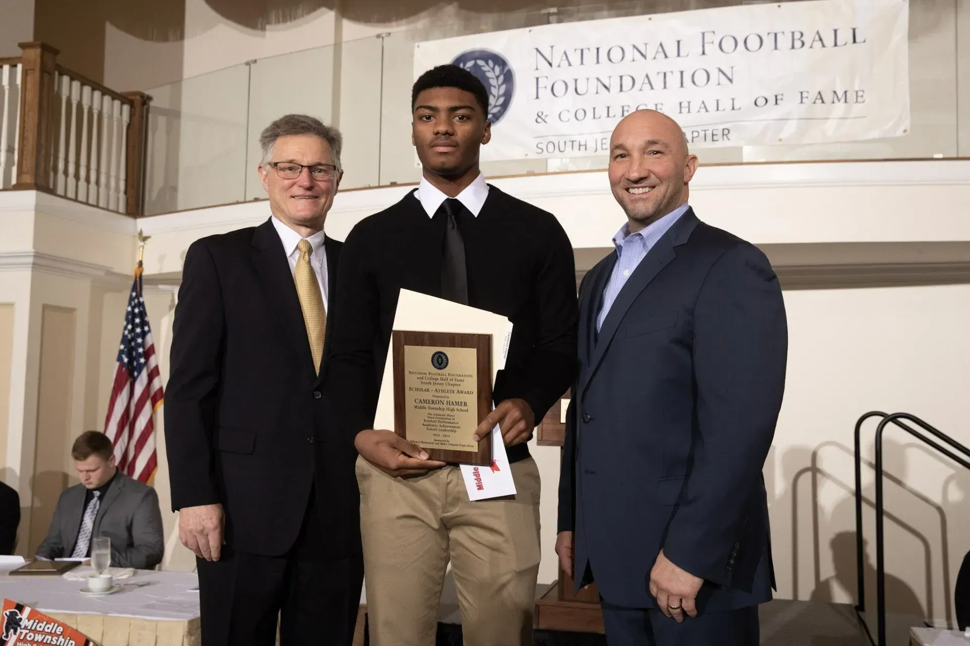 a man in a suit holds a plaque in front of a national football foundation banner