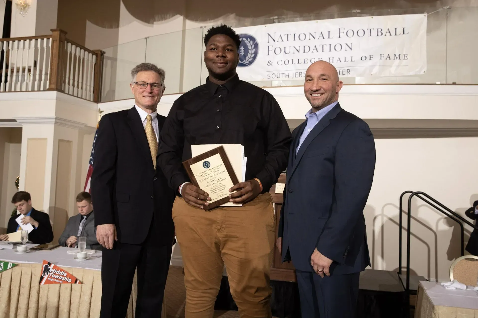 a man in a black shirt is holding a certificate in front of a sign that says national football foundation