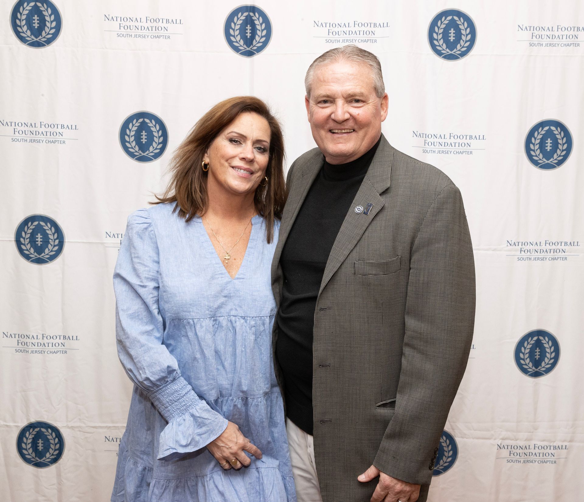 A man and a woman are posing for a picture in front of a backdrop
