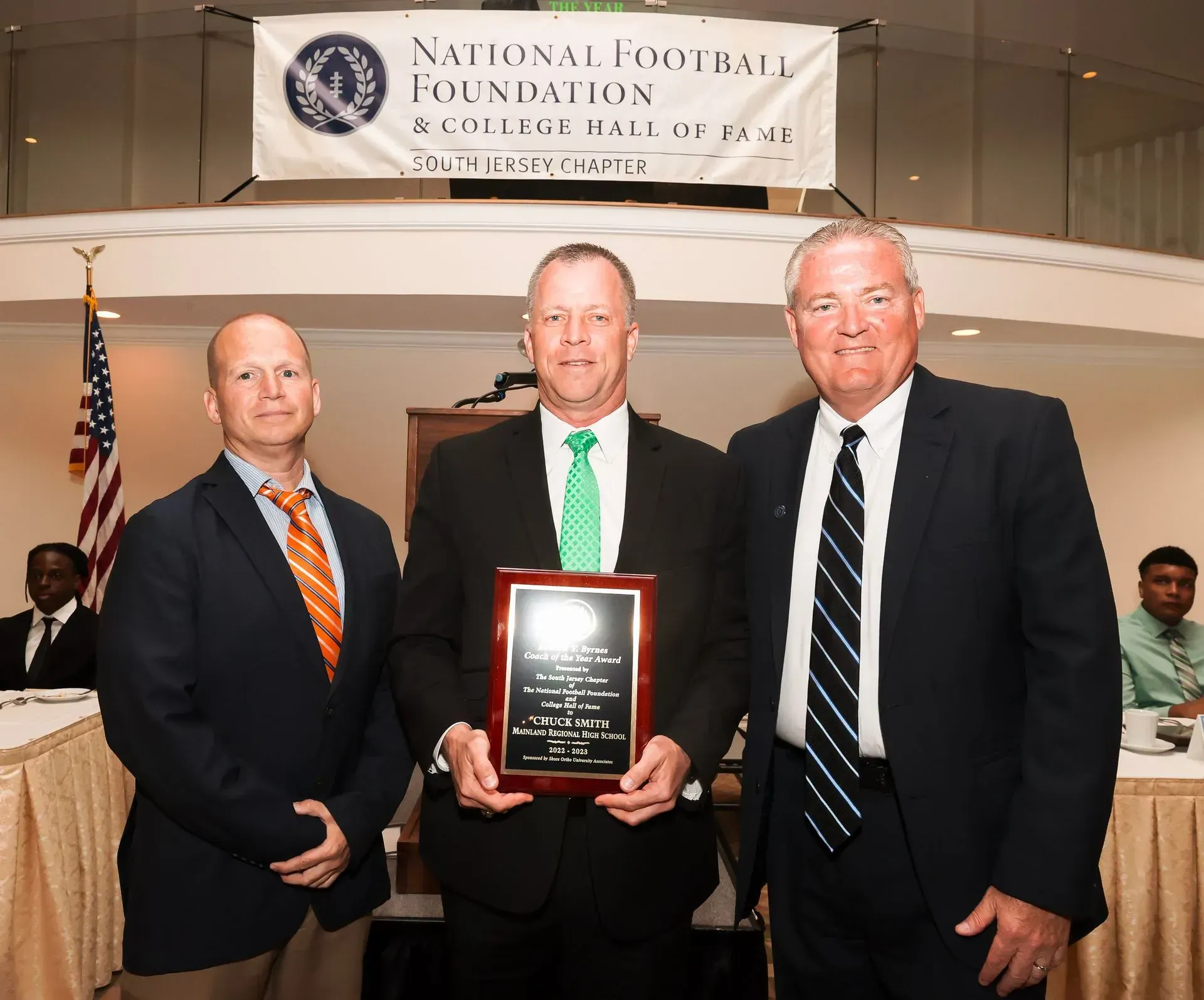 three men stand in front of a national football foundation banner