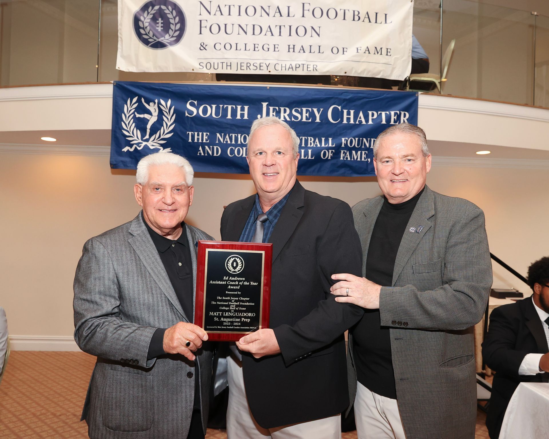 Three men are posing for a picture in front of a banner that says national football foundation south jersey chapter