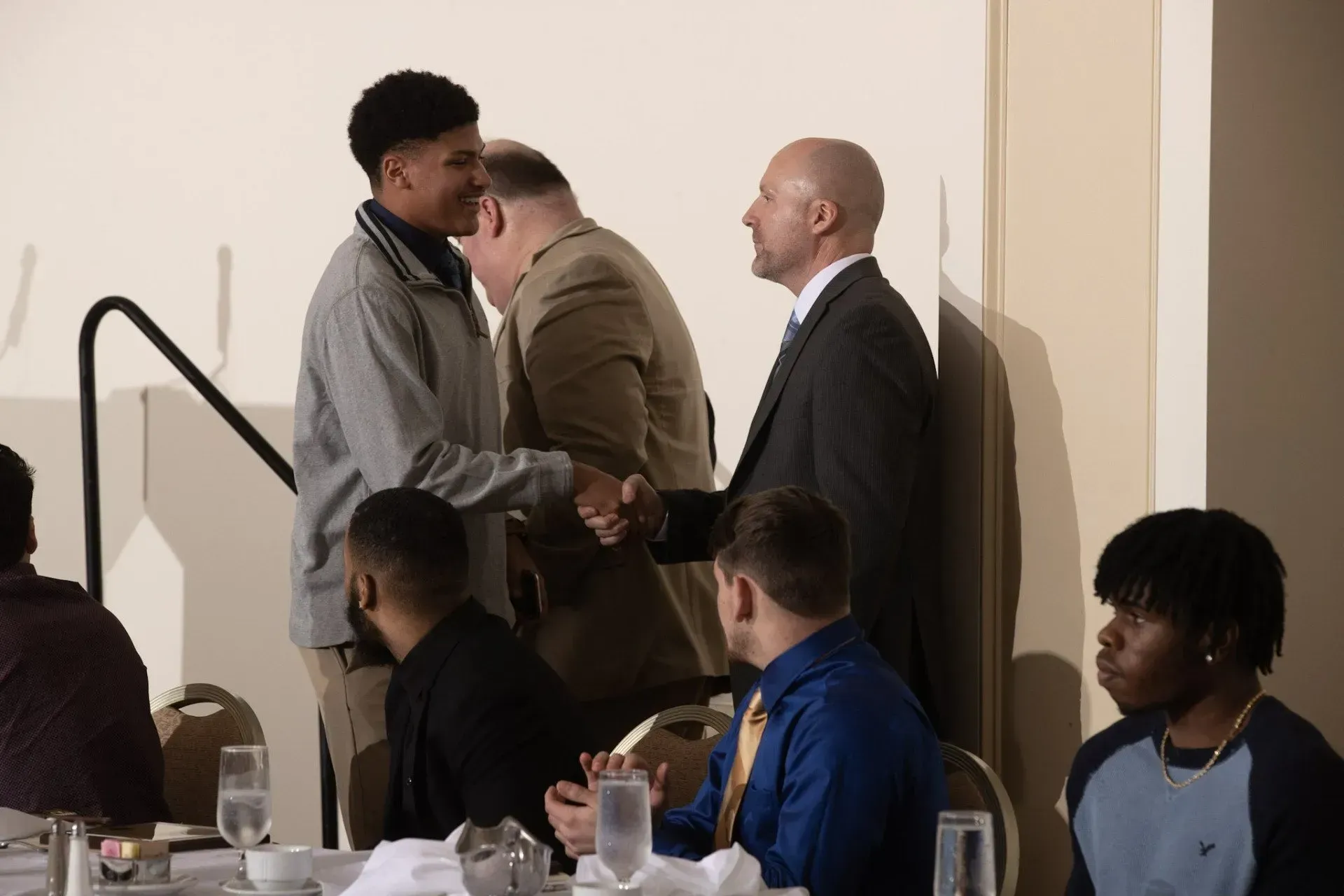 a group of people are sitting at a table shaking hands