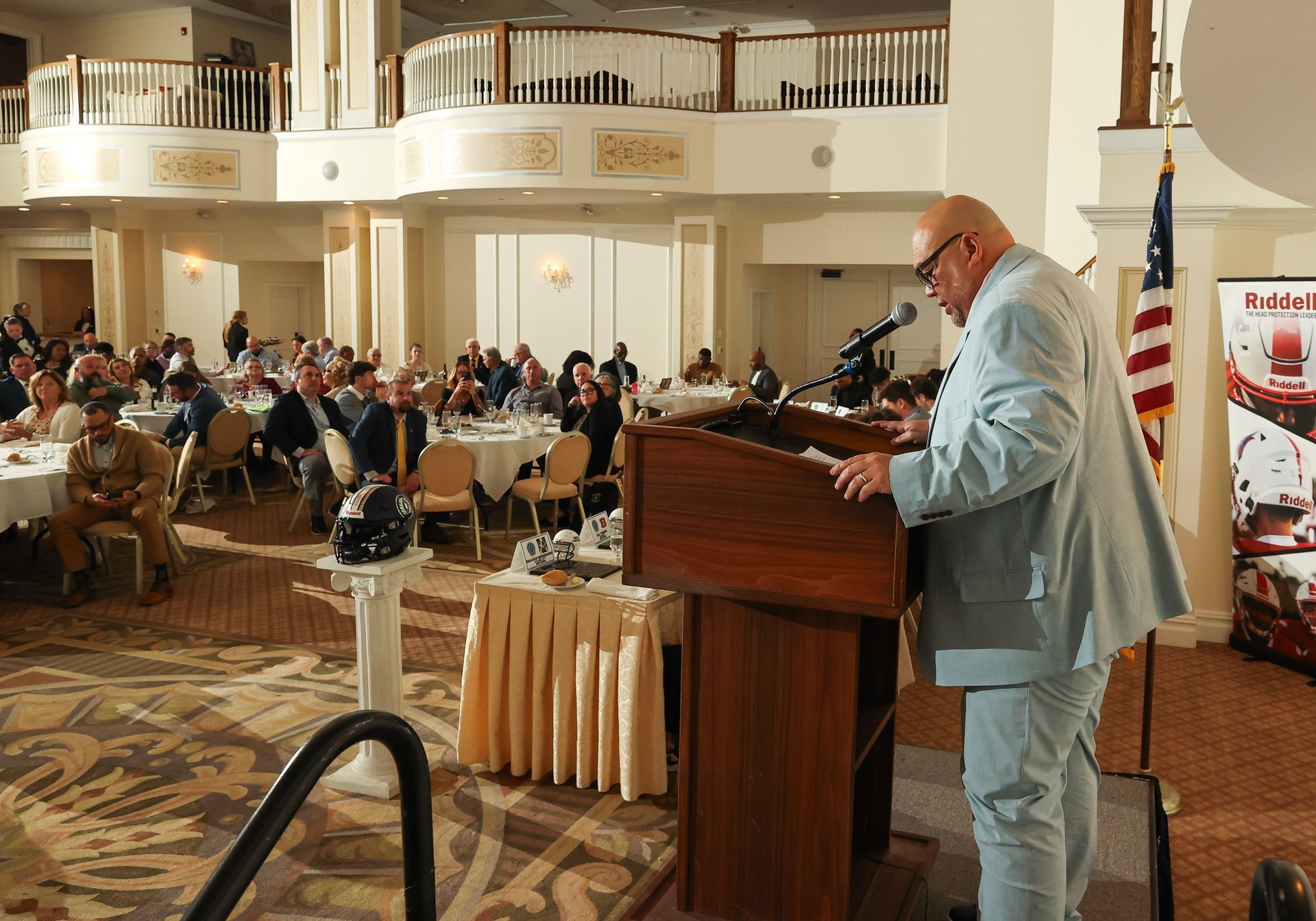 A man in a blue suit is standing at a podium speaking into a microphone