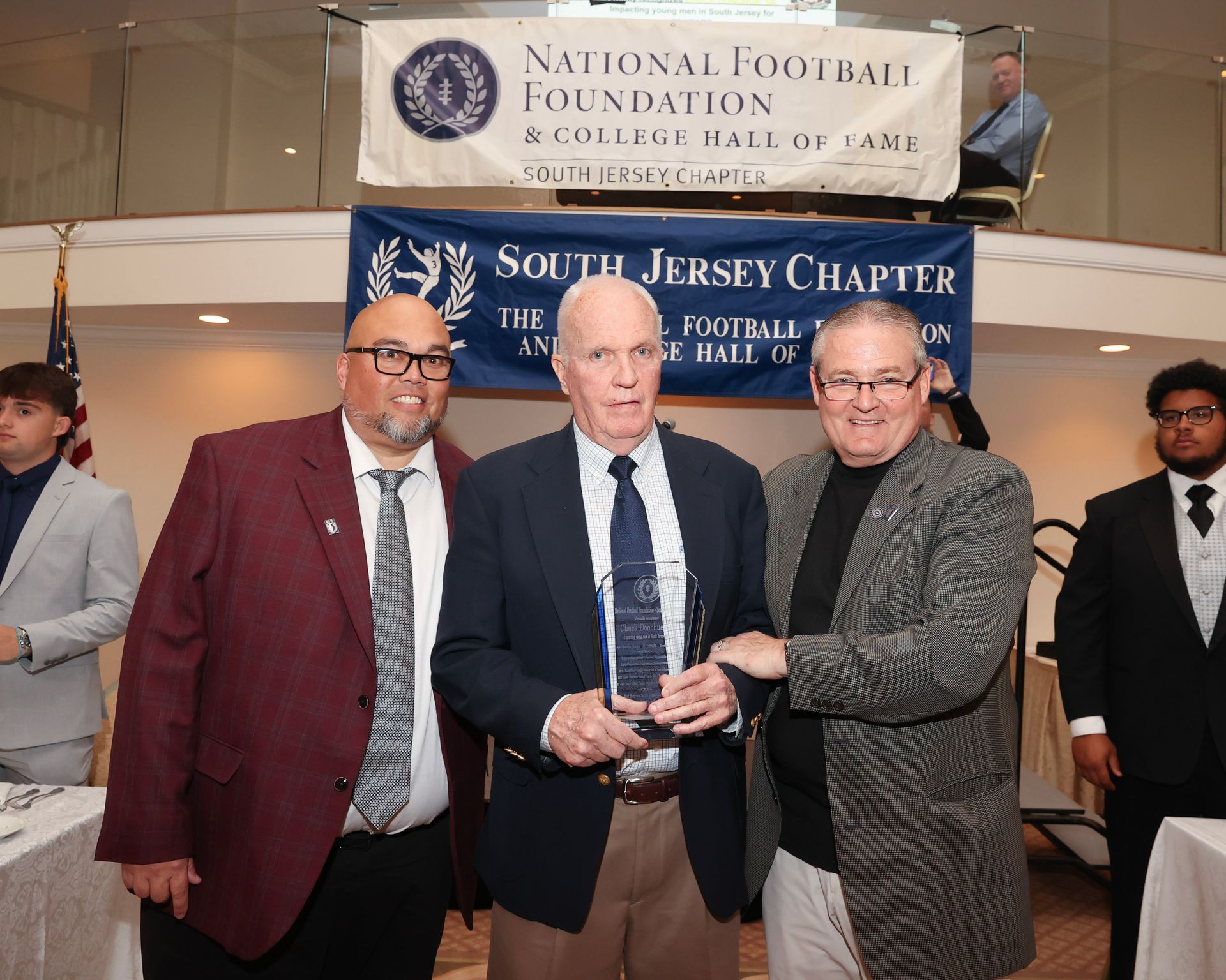 Three men are posing for a picture in front of a banner that says national football foundation south jersey chapter