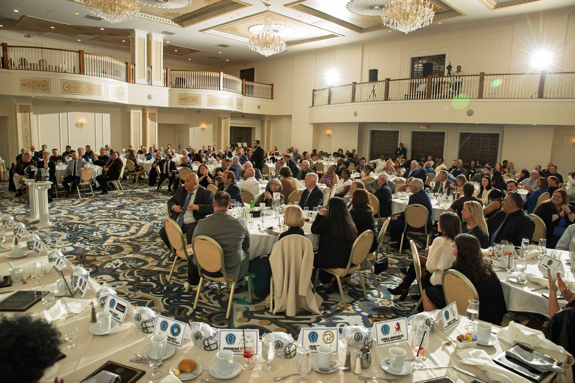 People gathered at round tables in a large, chandelier-lit banquet hall for a formal event