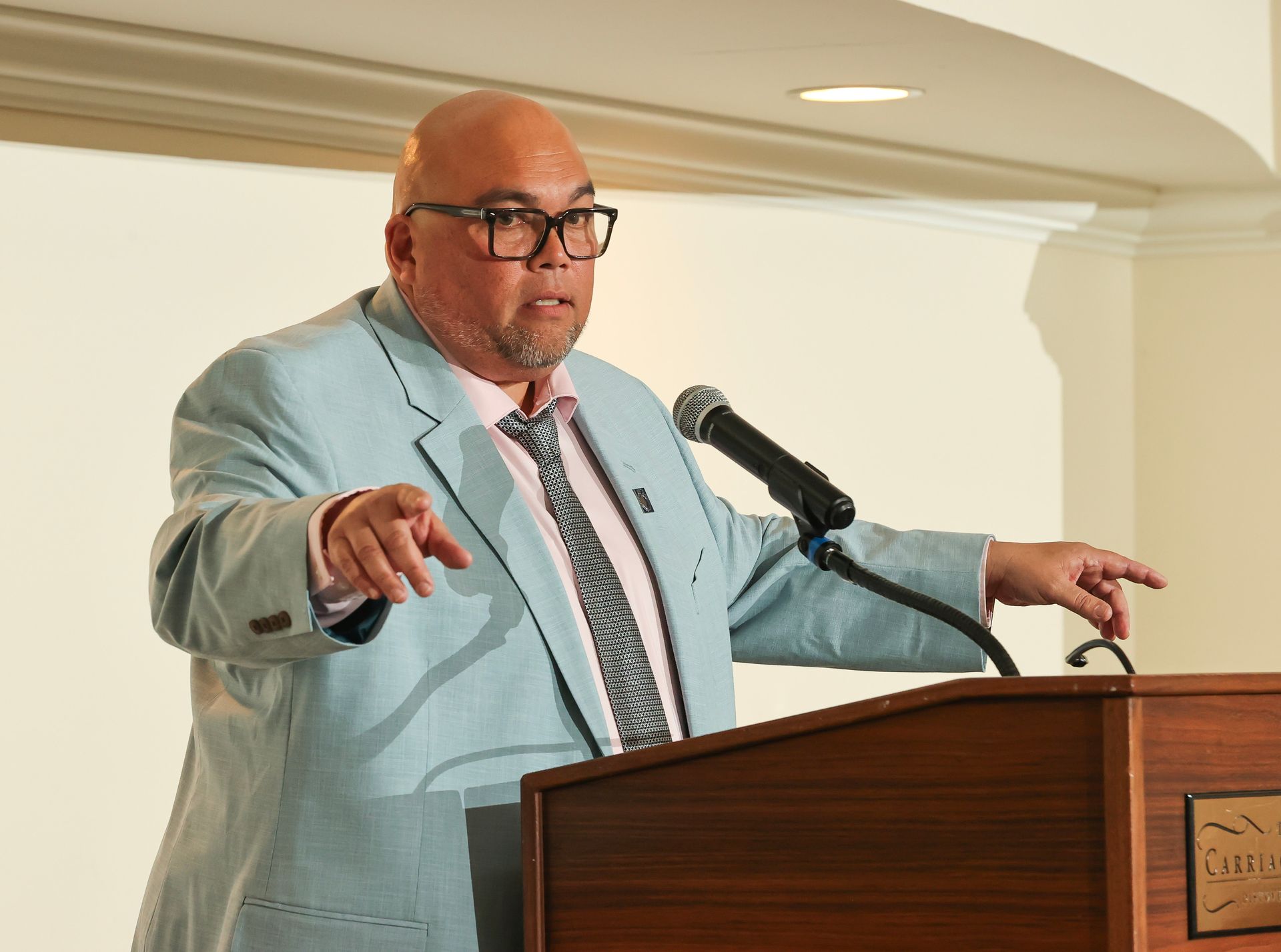 chuck donohue in a suit and tie is standing at a podium speaking into a microphone