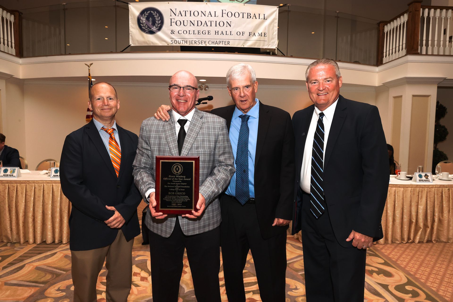 four men pose for a picture in front of a national football foundation banner
